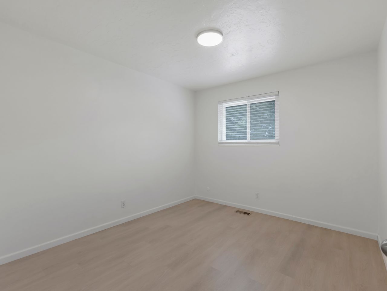 Bright room with light wood-finish flooring and a single window with blinds
