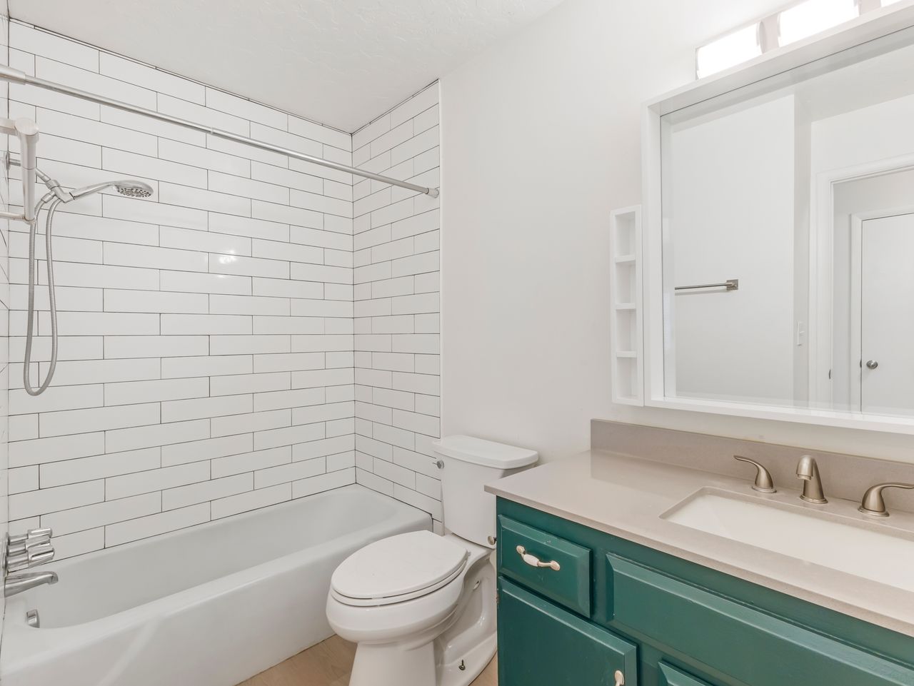 Bathroom featuring a white subway tile shower surround, a built-in tub, a vanity with a light-colored countertop, and a mirror with integrated shelving