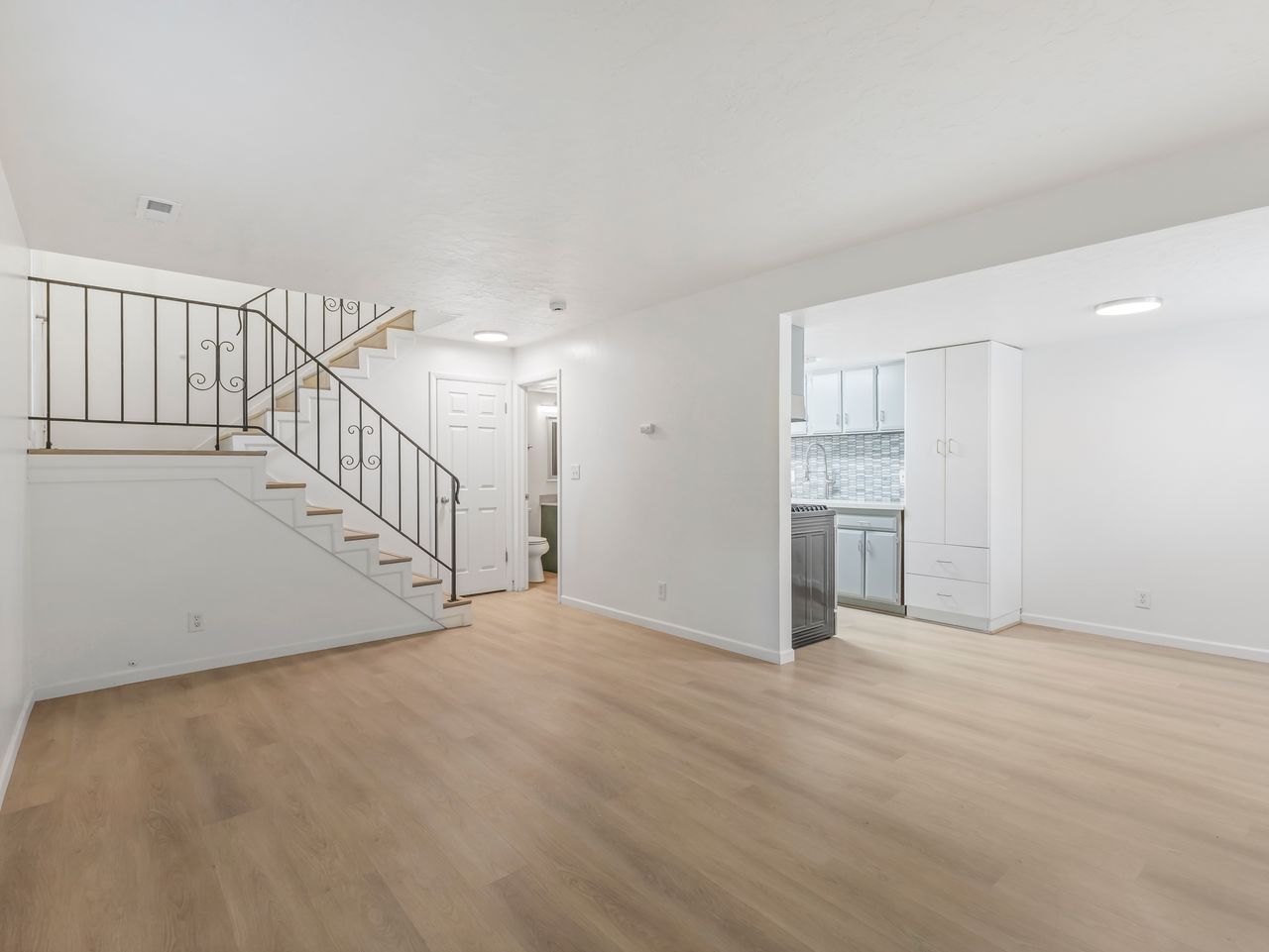 Open-concept living area with wood-finish flooring, a staircase featuring a wrought iron railing, and recessed ceiling lights