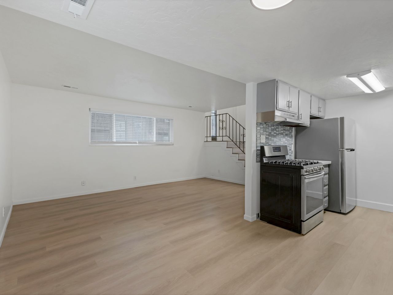 Open-concept living area featuring wood-finish flooring, a contemporary kitchen with stainless steel appliances, and a tiled backsplash