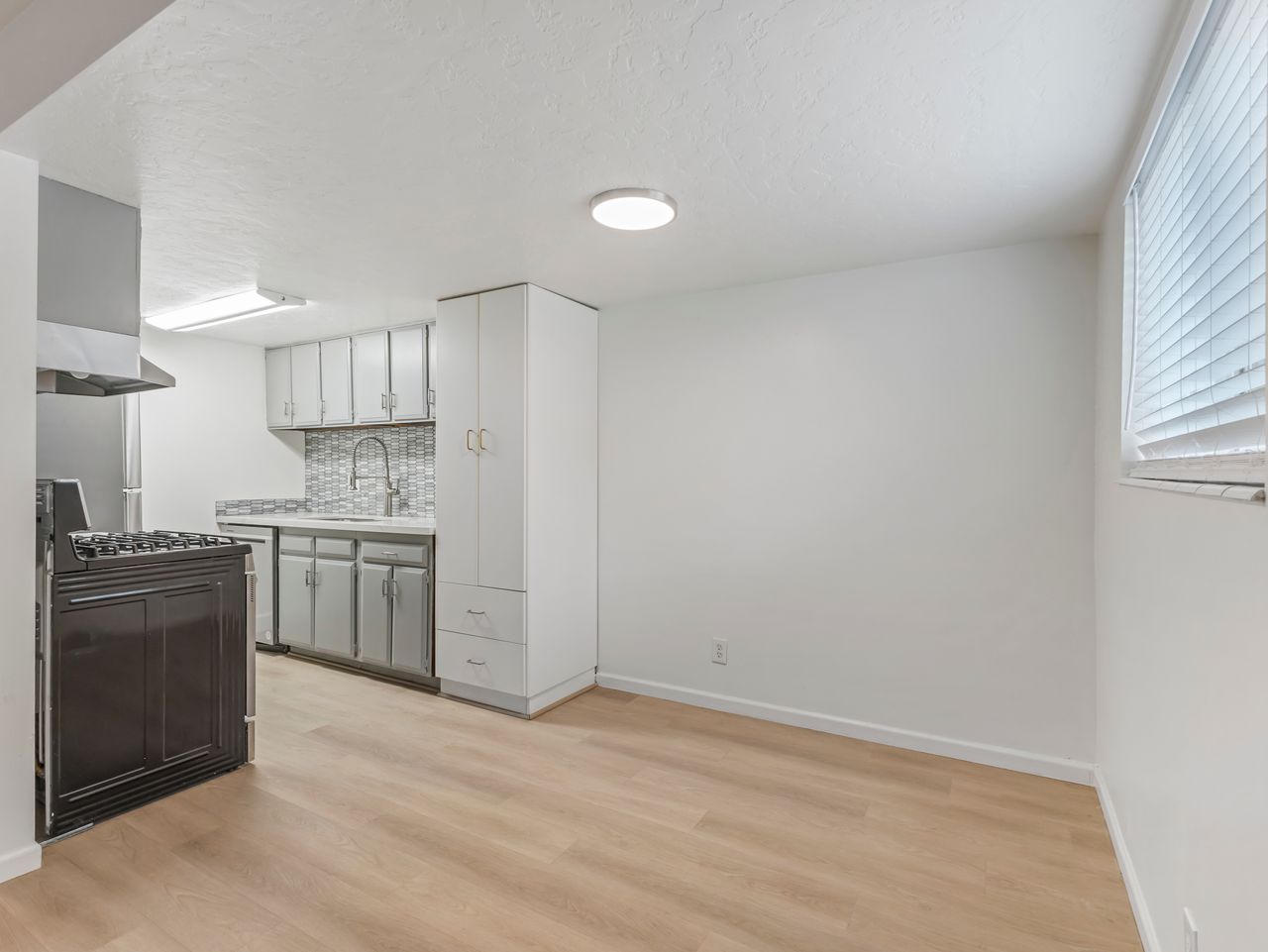 Kitchen area featuring light wood-finish flooring, white cabinetry, and a textured backsplash