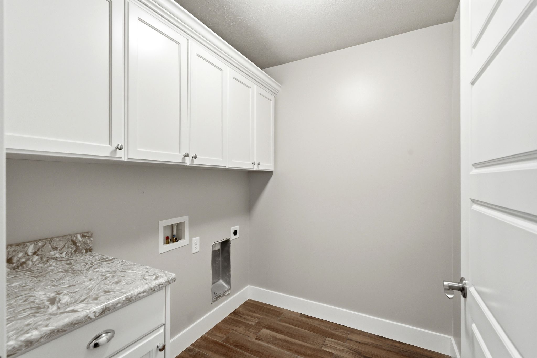Laundry room featuring white shaker cabinetry, patterned countertop, and wood-finish flooring