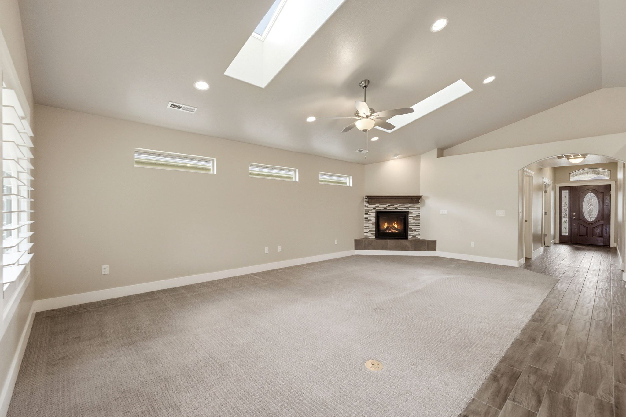 Spacious living area featuring a corner fireplace with stone surround and wood mantel, vaulted ceiling with skylights, recessed lighting, and a ceiling fan