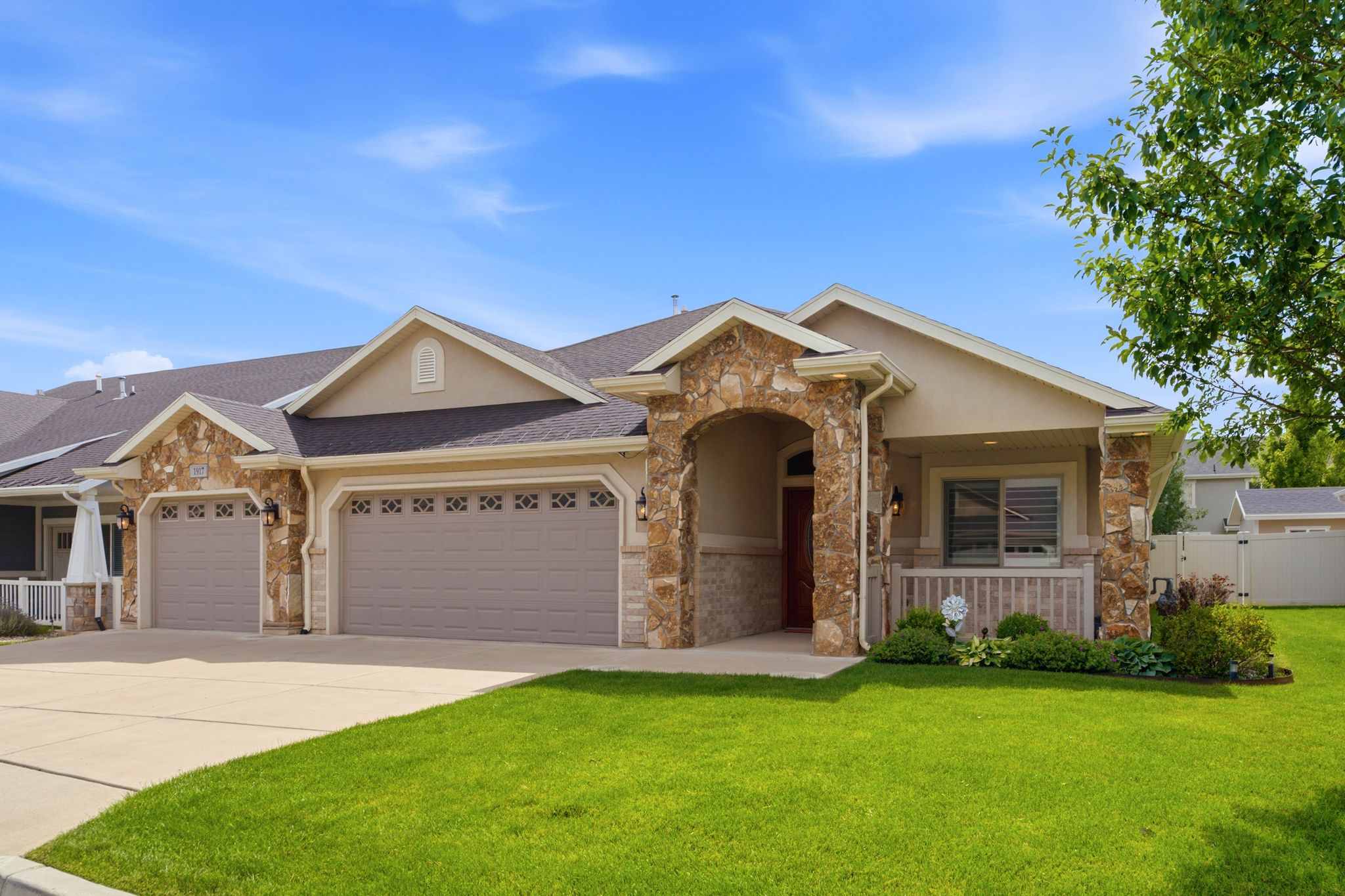 Stone and stucco exterior featuring an arched entry, covered front porch, and a two-car garage