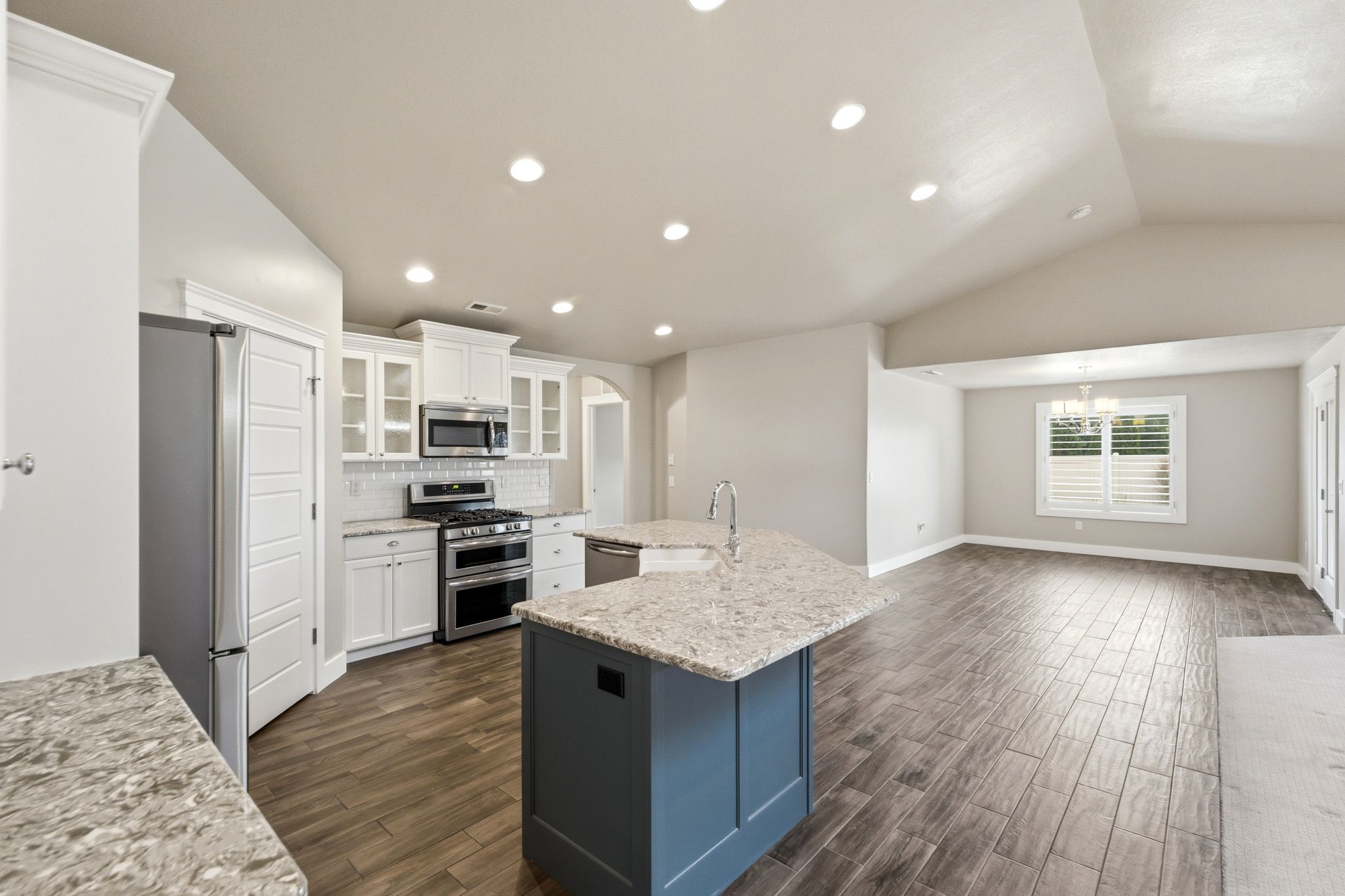 Modern kitchen featuring an expansive island with a light-toned countertop, stainless steel appliances, white cabinetry, and wood-finish flooring