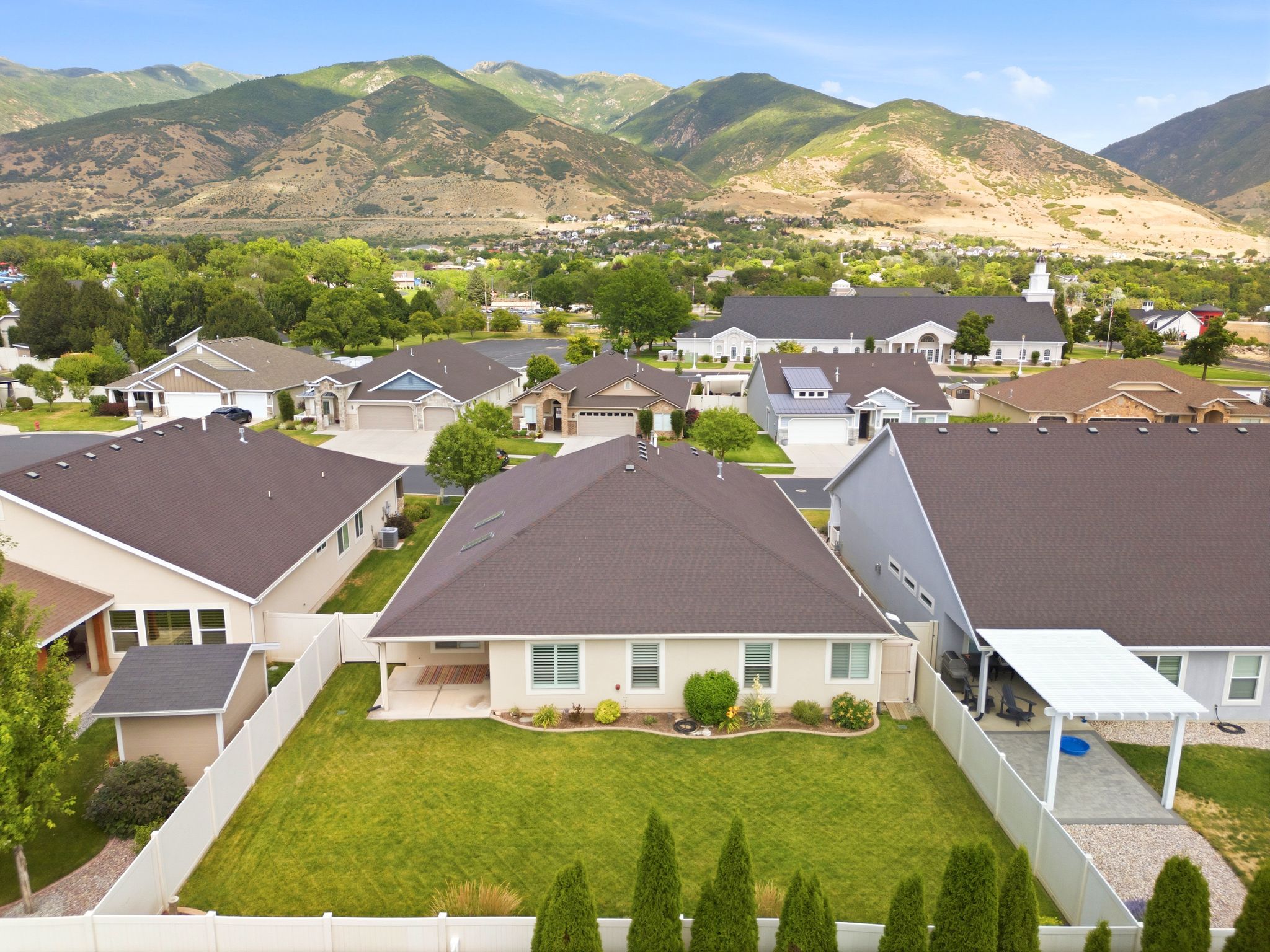 Expansive backyard featuring a manicured lawn, white vinyl fencing, and mature landscaping