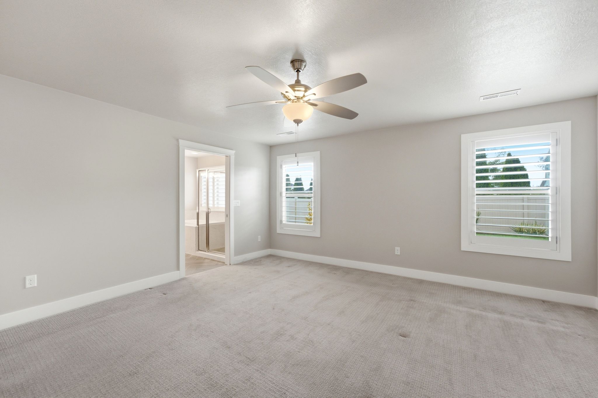 Spacious room featuring light gray carpeting, neutral wall finishes, and a ceiling fan with integrated lighting