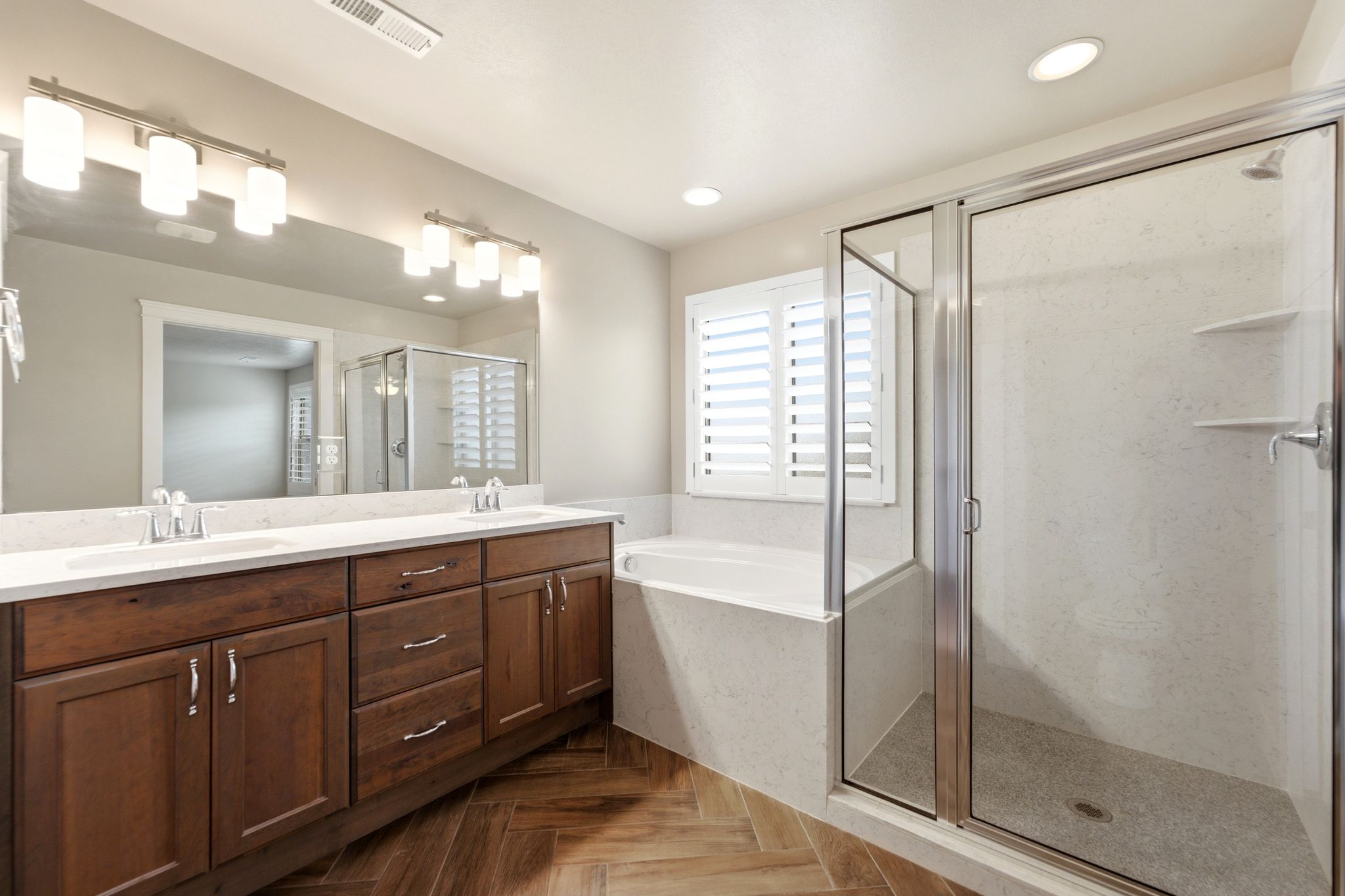 Bathroom featuring a dual vanity with wood-finish cabinetry, a large frameless mirror, and overhead linear light fixtures