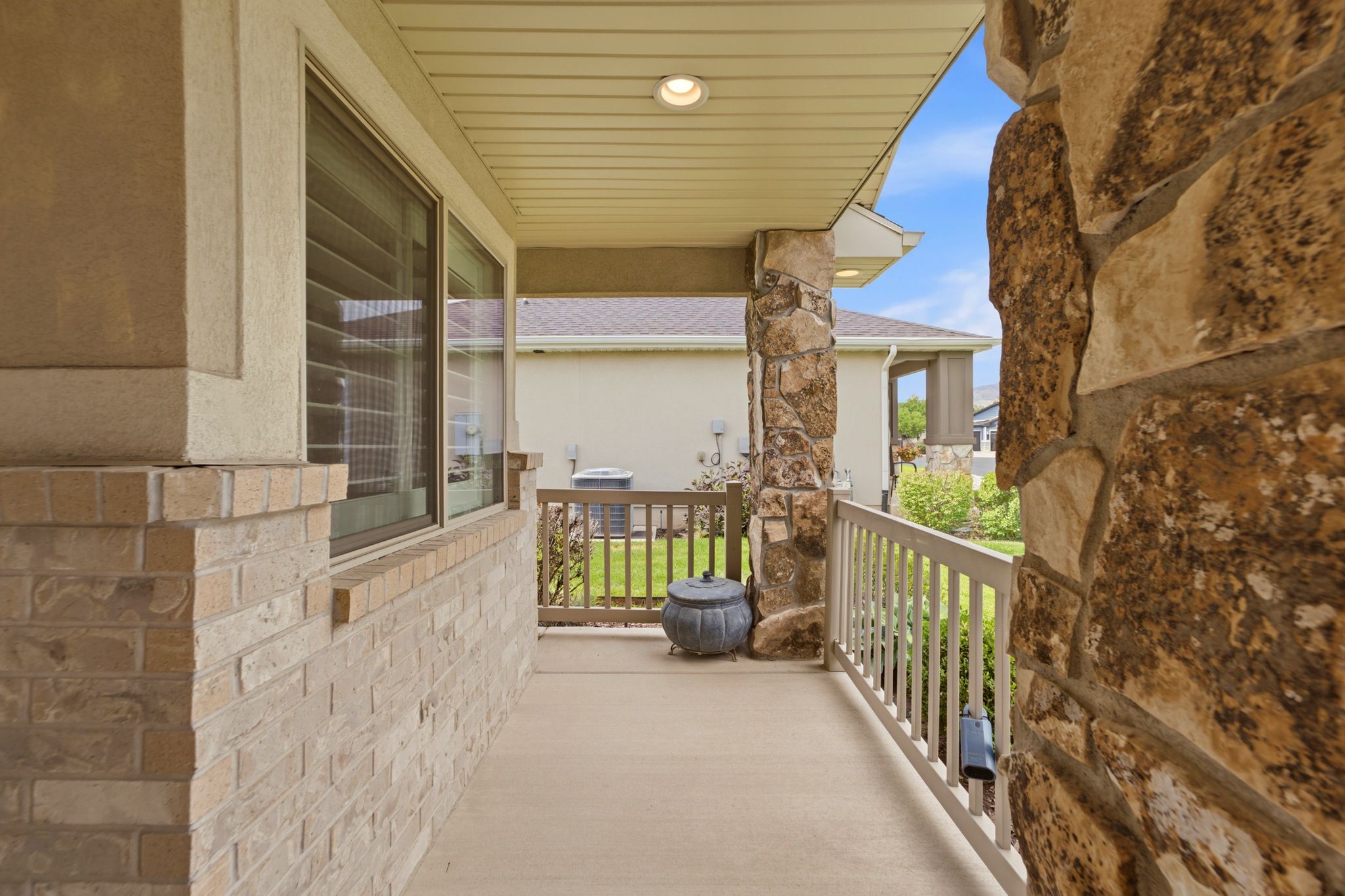 Covered porch featuring a natural stone accent wall and column, brick facade, and a painted wood railing