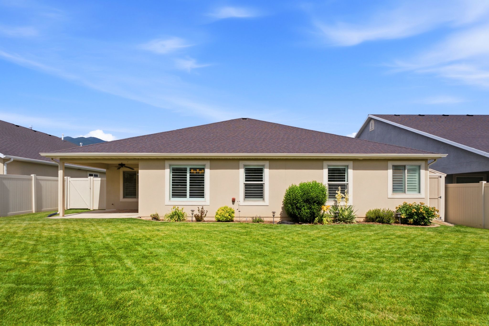 Expansive grassy lawn with a covered patio featuring a ceiling fan