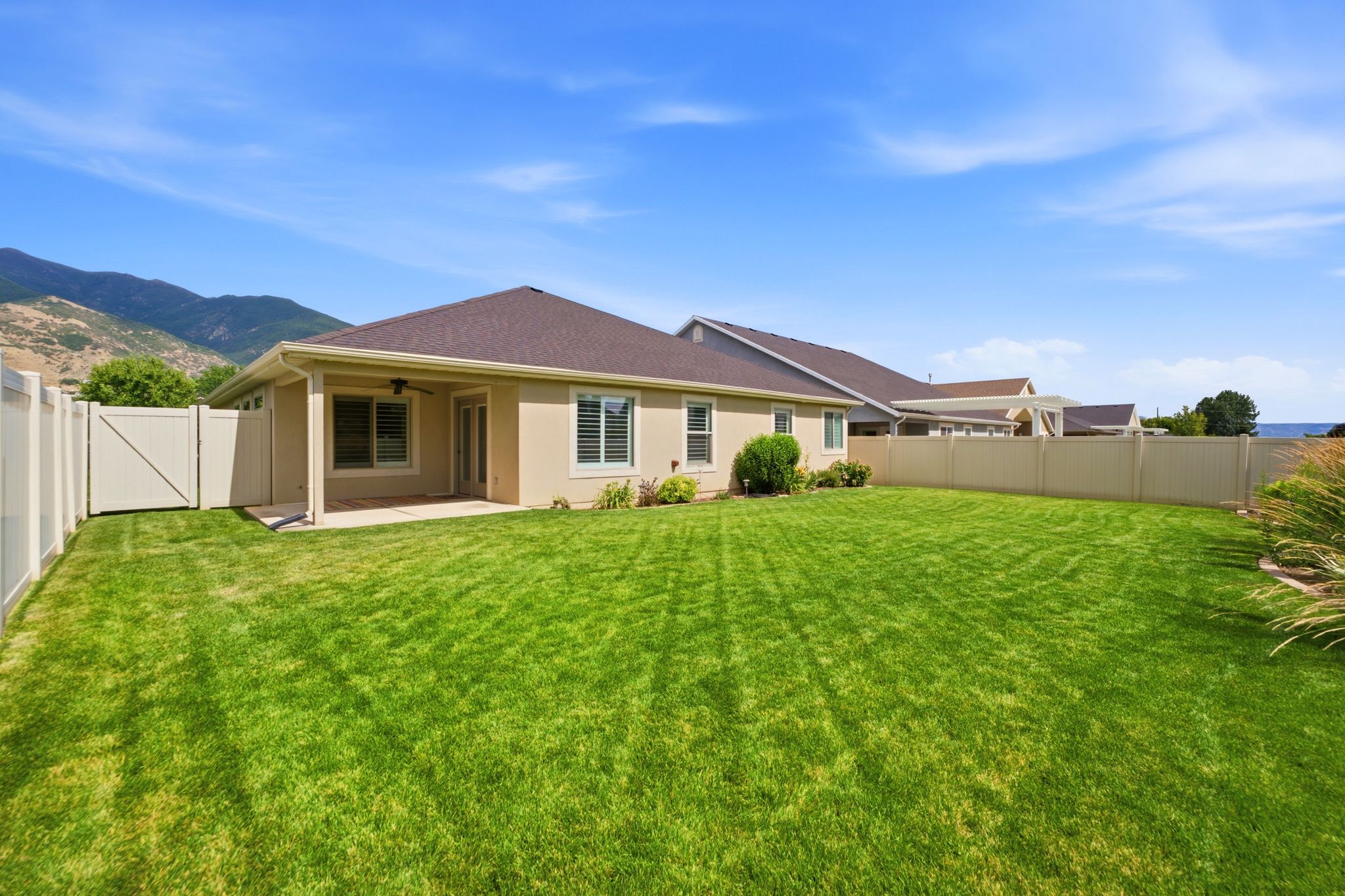 Expansive fenced backyard featuring a substantial lawn, a covered patio area, and a privacy fence