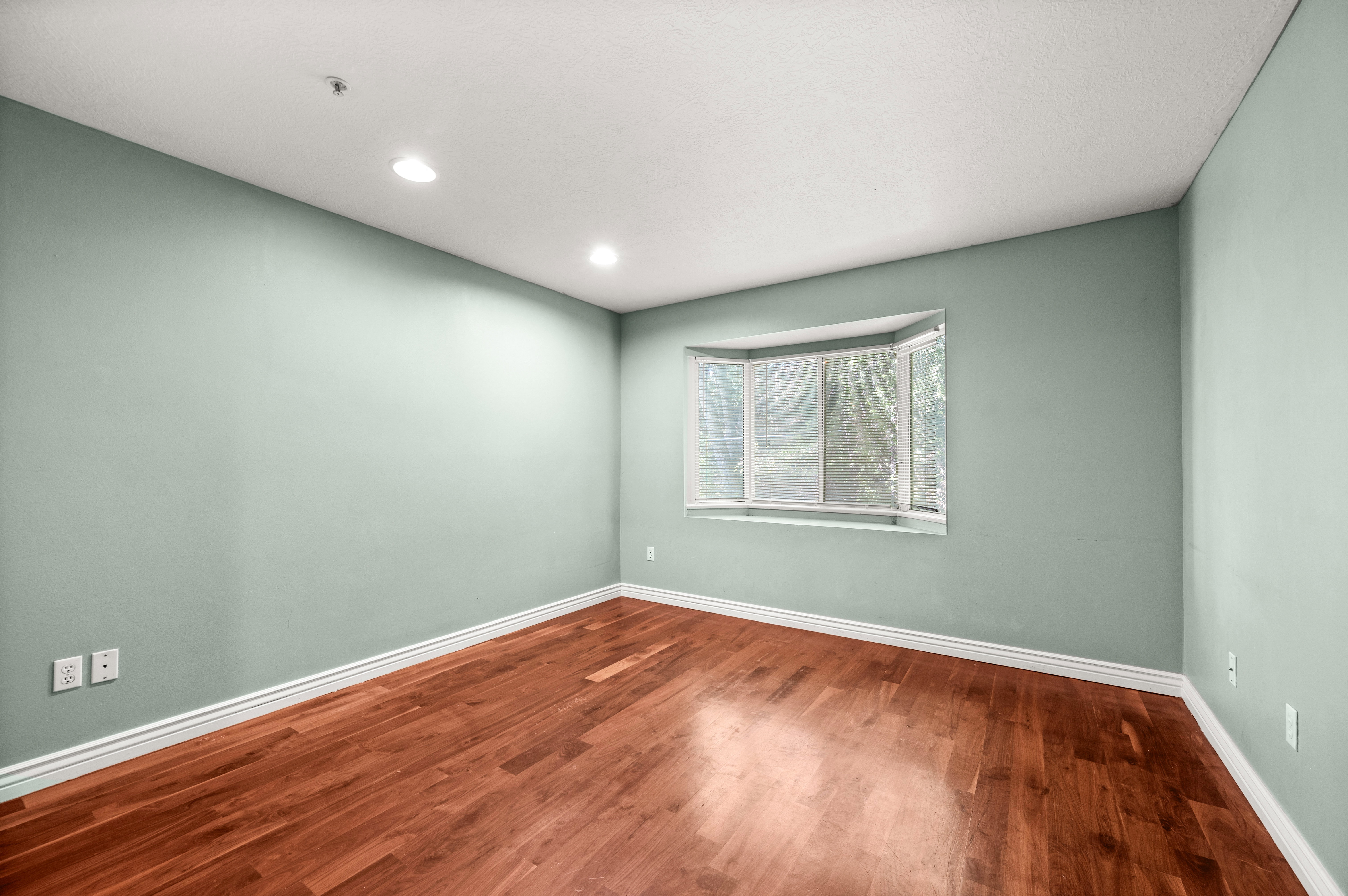 Room featuring wood-finish flooring, light green walls, a bay window, recessed lighting, and white baseboards