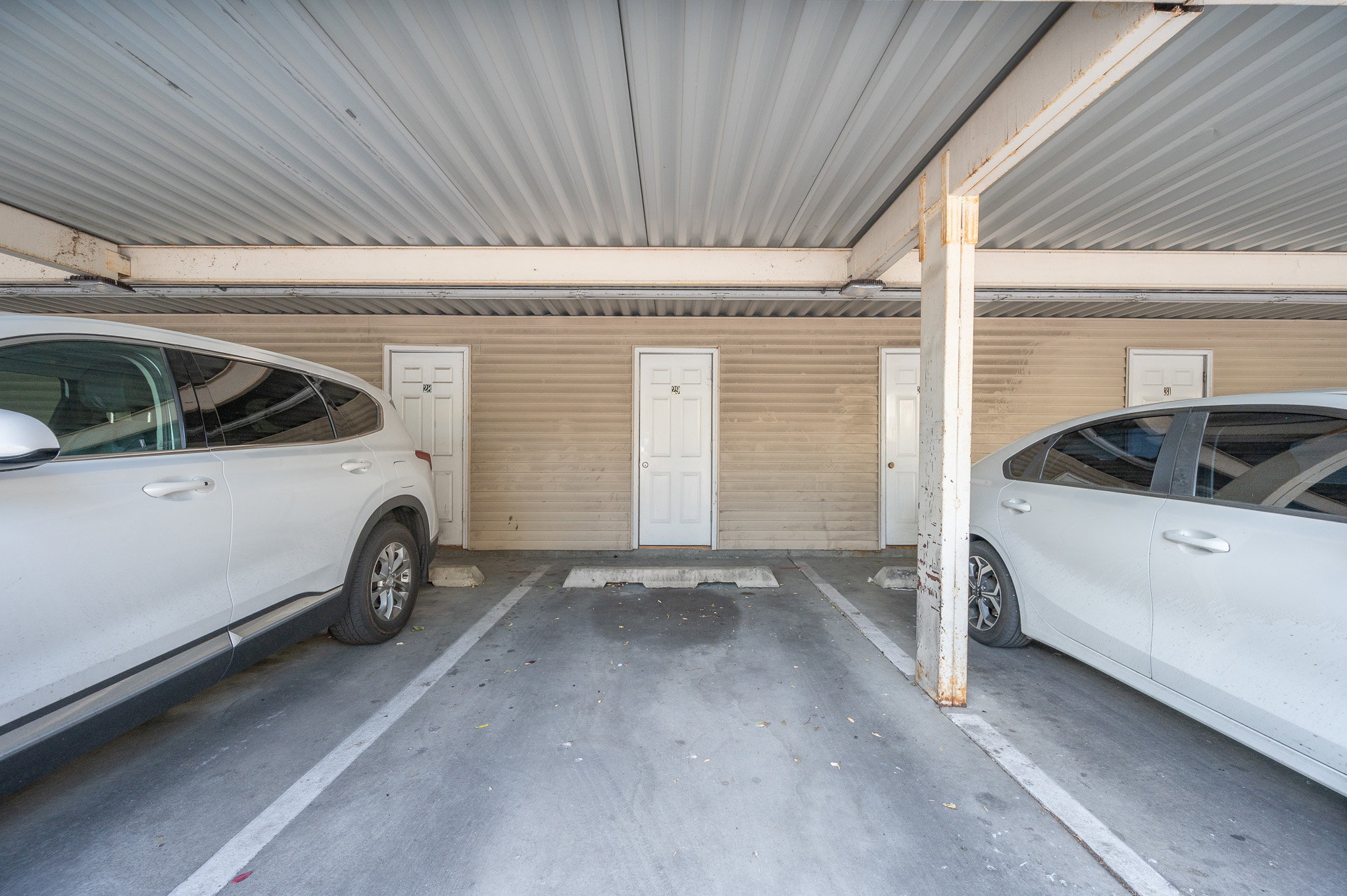 Covered parking area featuring concrete flooring and a corrugated metal ceiling