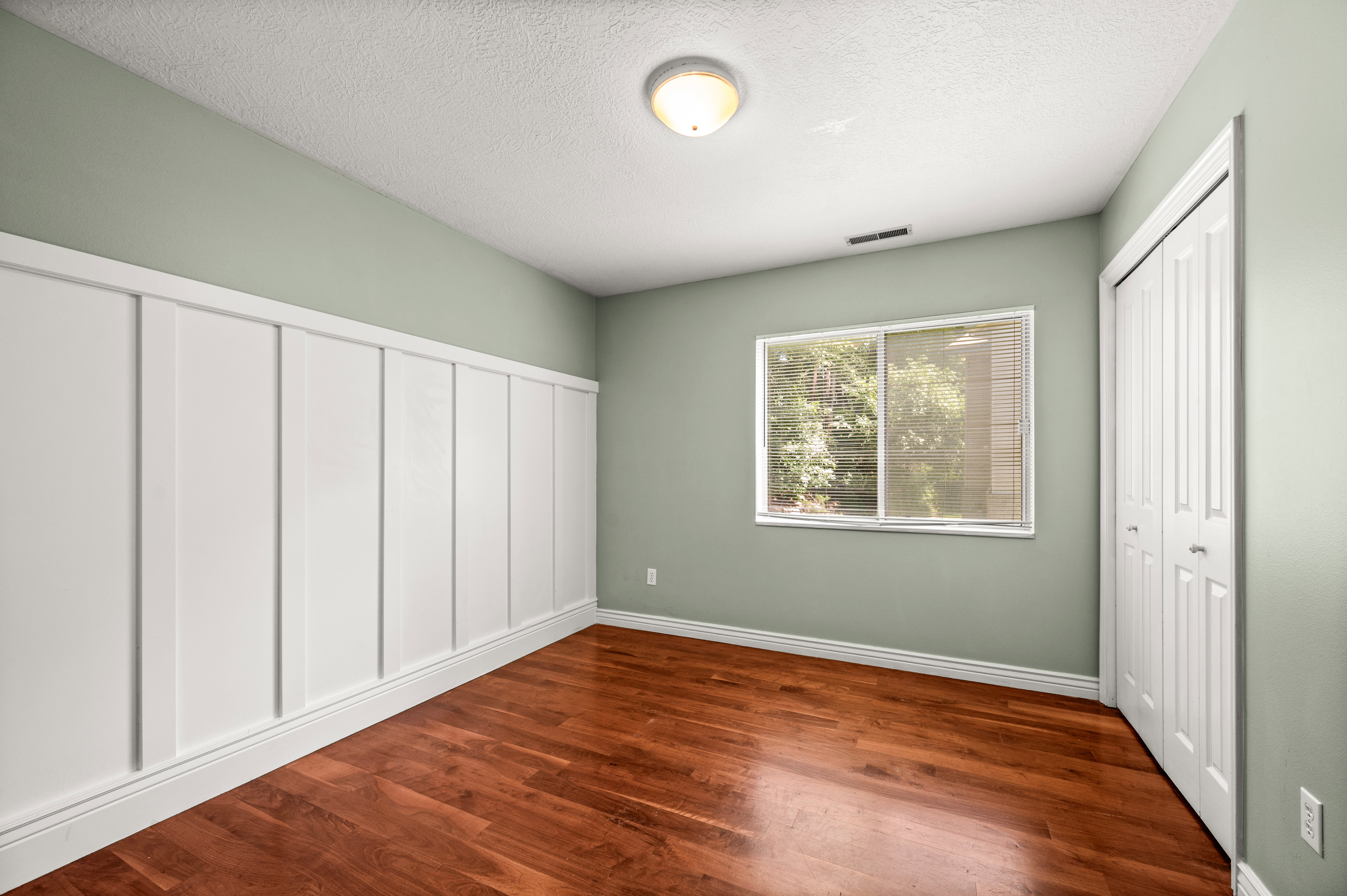 Bedroom featuring wood-finish flooring, a board and batten accent wall, neutral painted walls, and a bi-fold closet
