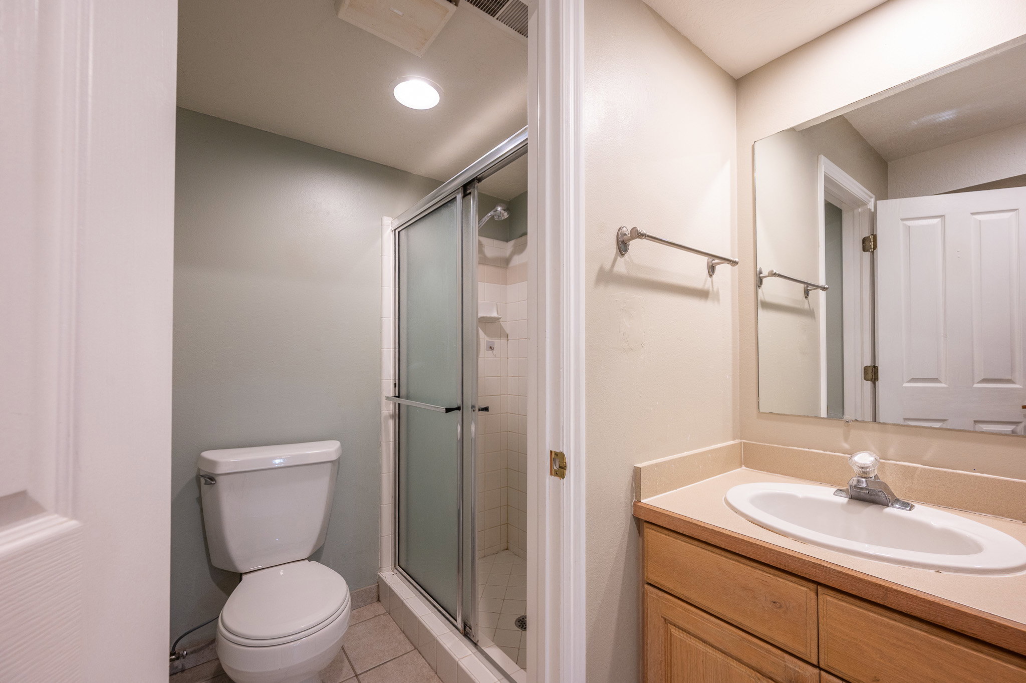 Full bathroom featuring a single vanity with a laminate countertop, a framed mirror, and a shower with a sliding glass enclosure
