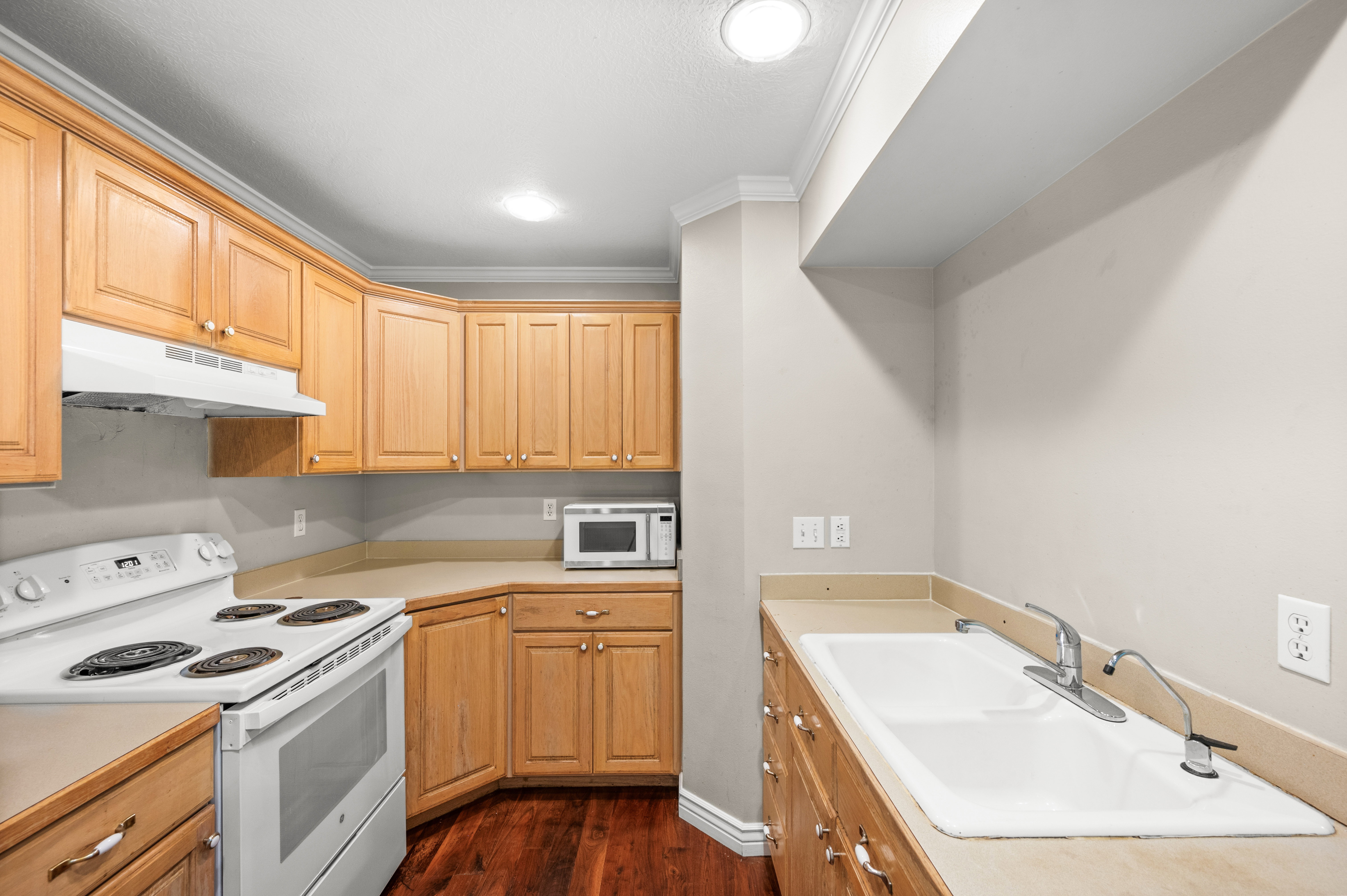 Kitchenette featuring wood-finish cabinetry, a white electric range with range hood, and a built-in double basin sink