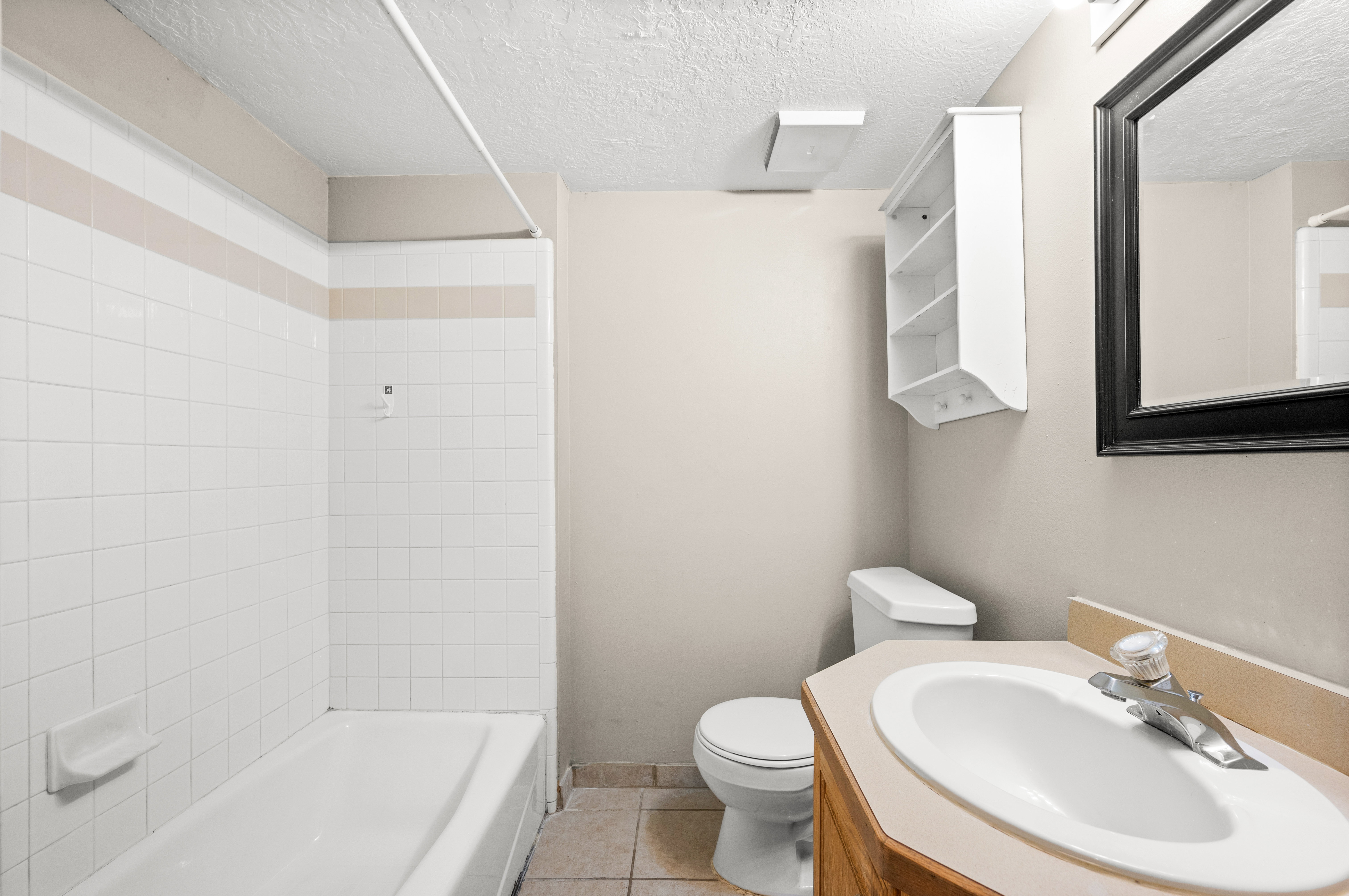 Bathroom featuring a white bathtub with subway tile surround, neutral-toned walls, a vanity with a laminate countertop, and a framed mirror
