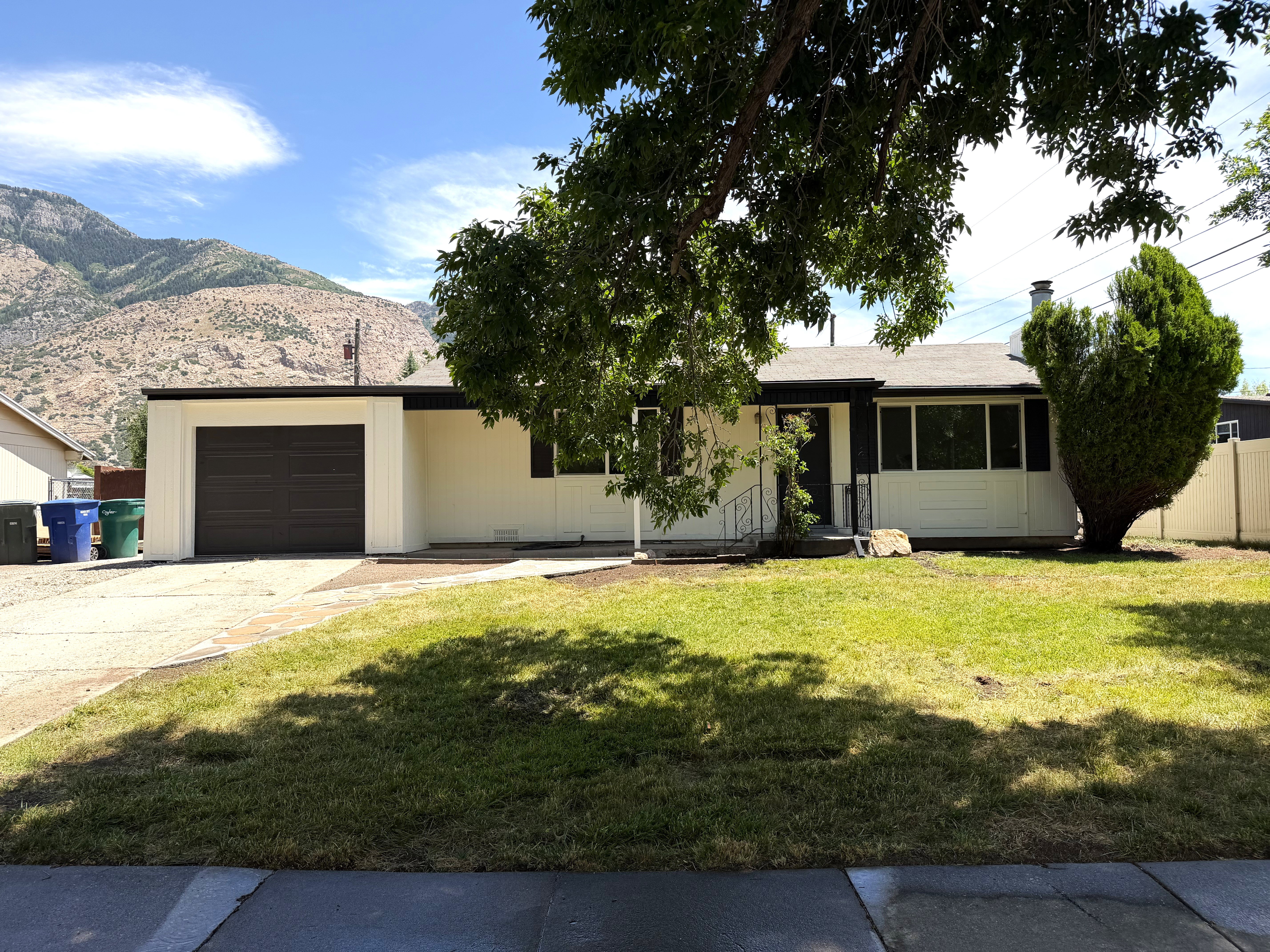 Ranch-style residence featuring a prominent mountain backdrop, an attached garage with a dark wood-finish door, a front lawn, and a paved driveway