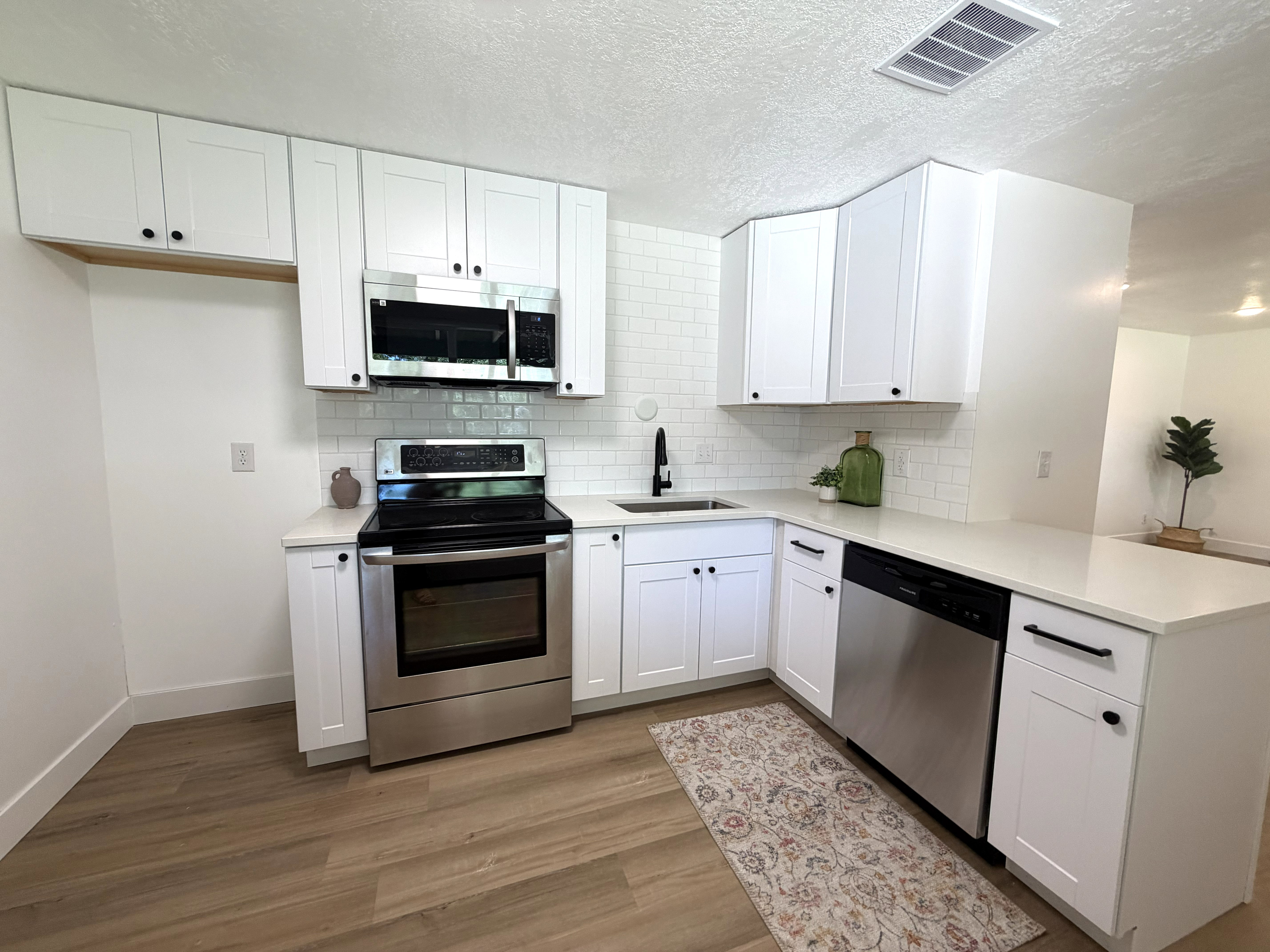Kitchen featuring white cabinetry, stainless steel appliances, white subway tile backsplash, light-toned countertops, and wood-finish flooring