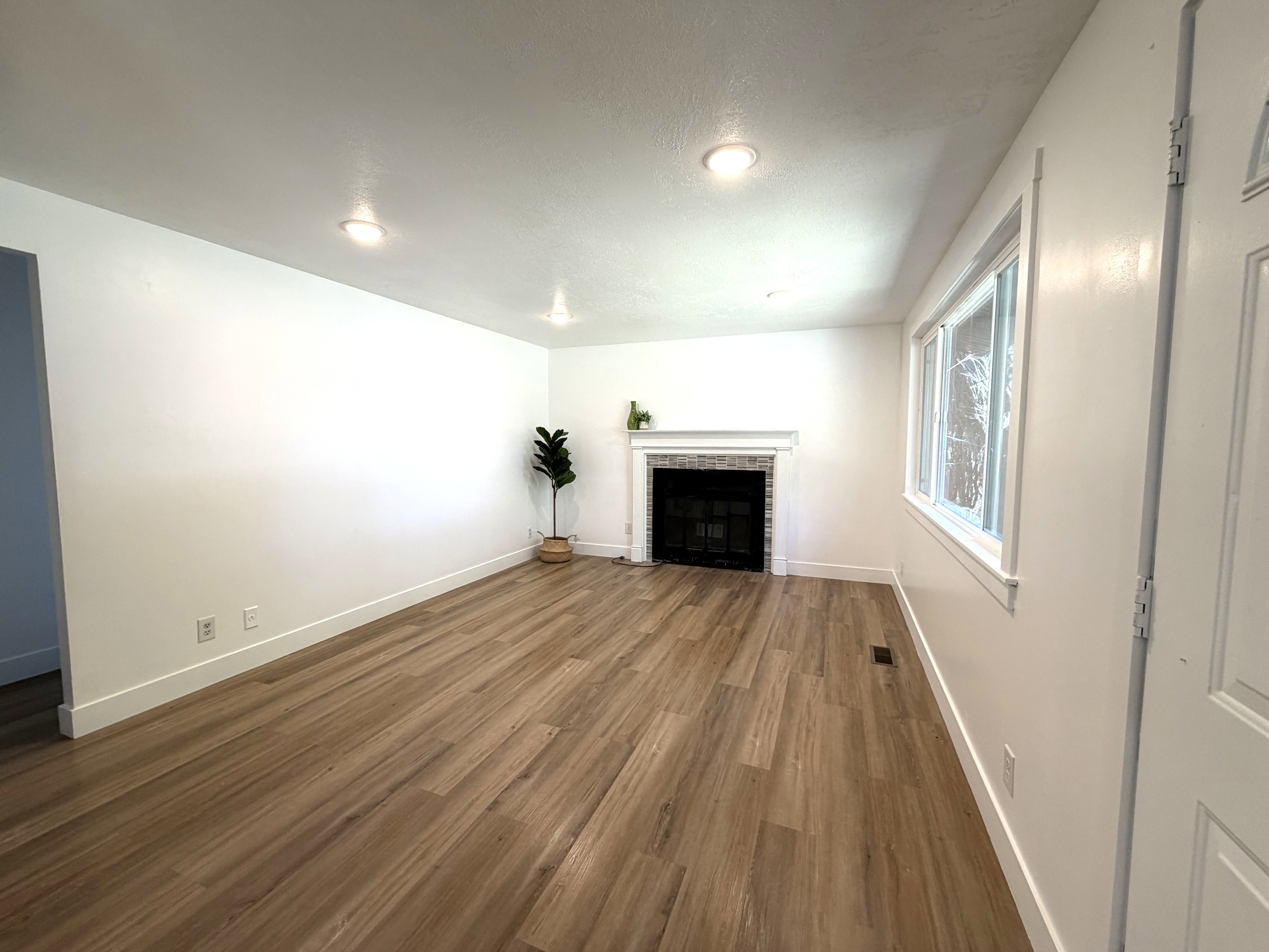 Bright living space featuring wood-finish flooring, recessed lighting, and a white fireplace with a tiled surround