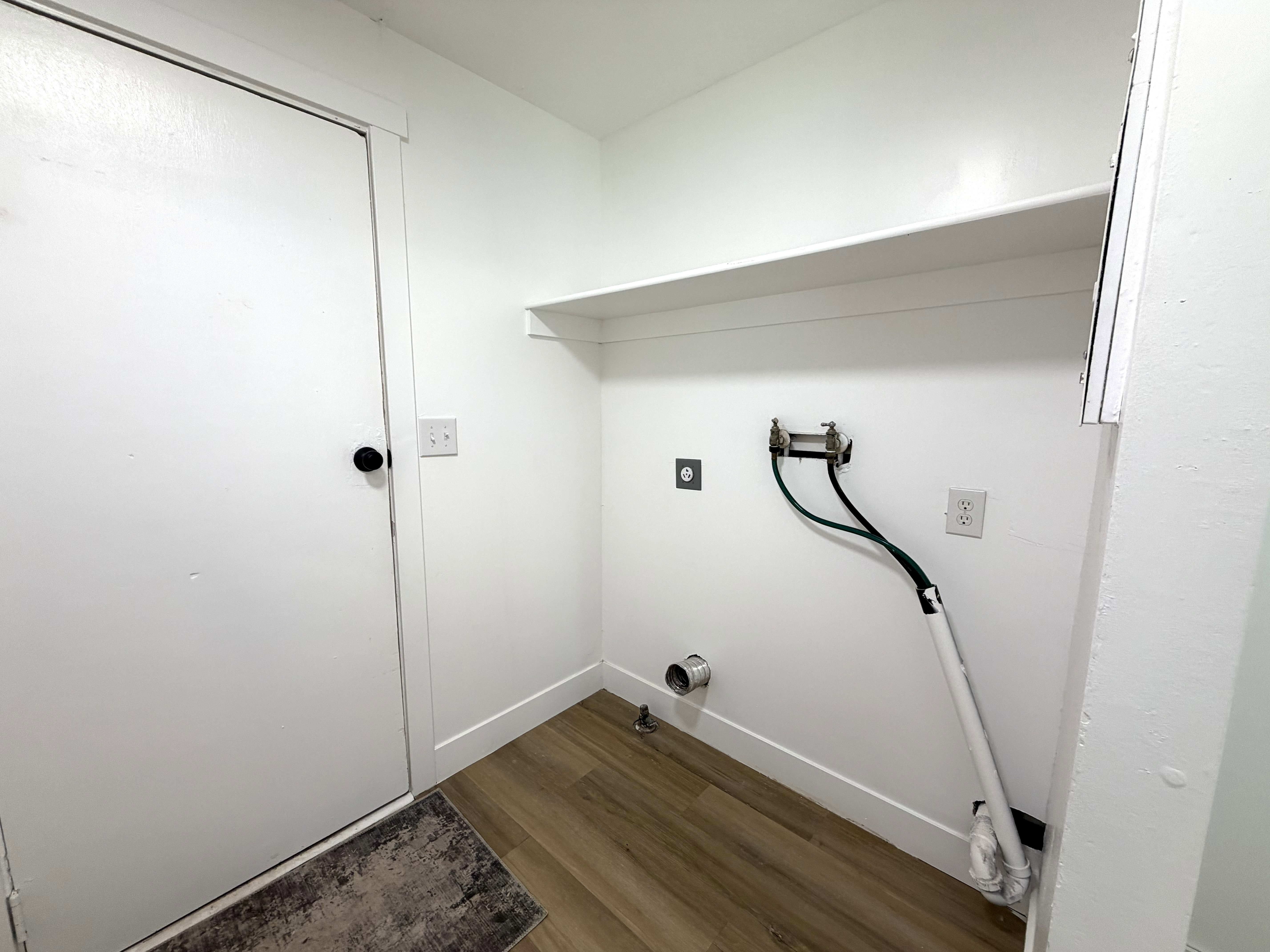 Dedicated laundry area featuring wood-finish flooring, a built-in shelf, and appliance hookups