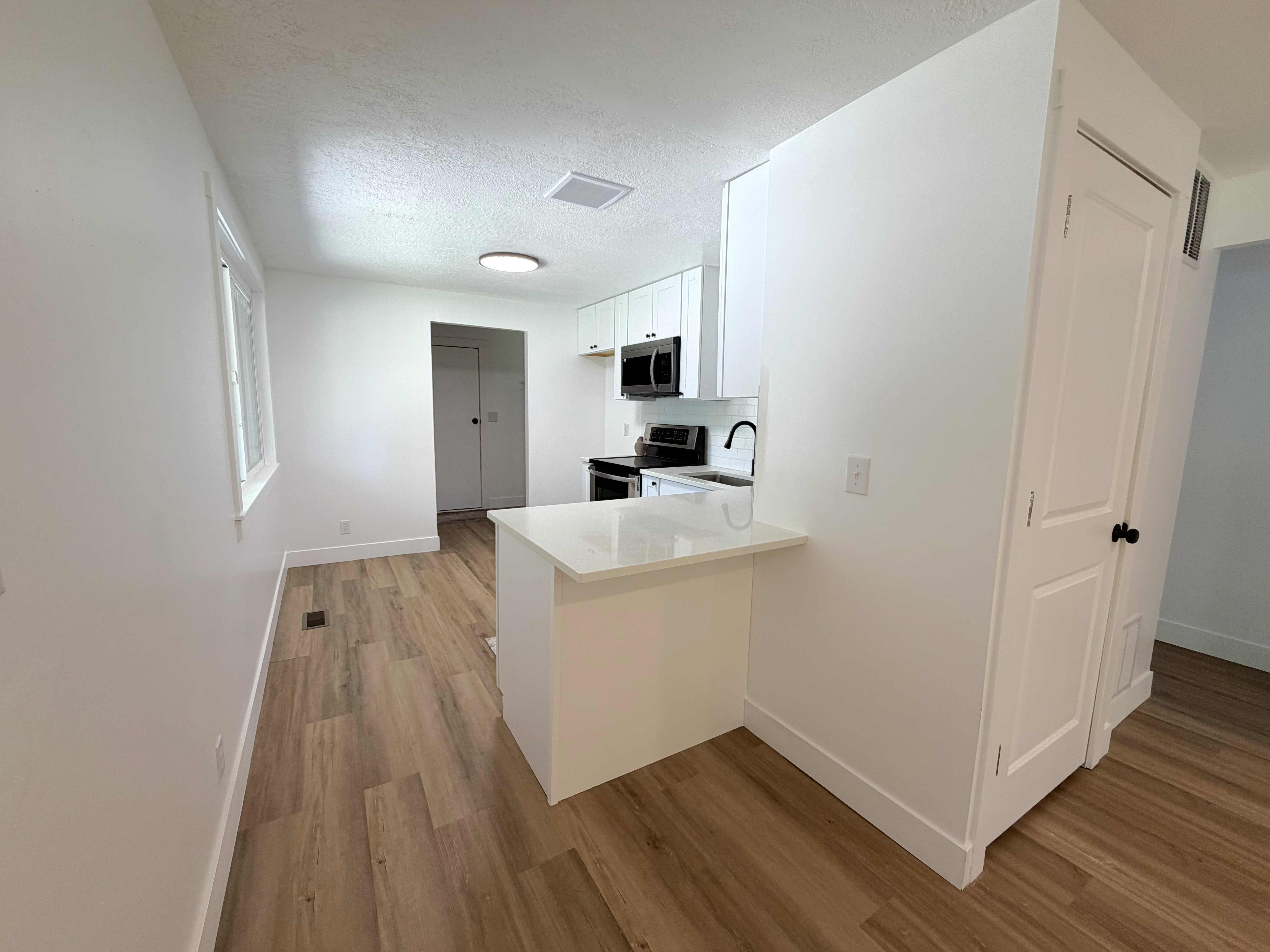 Contemporary kitchen featuring white cabinetry, black appliances, a white countertop peninsula, and wood-finish flooring