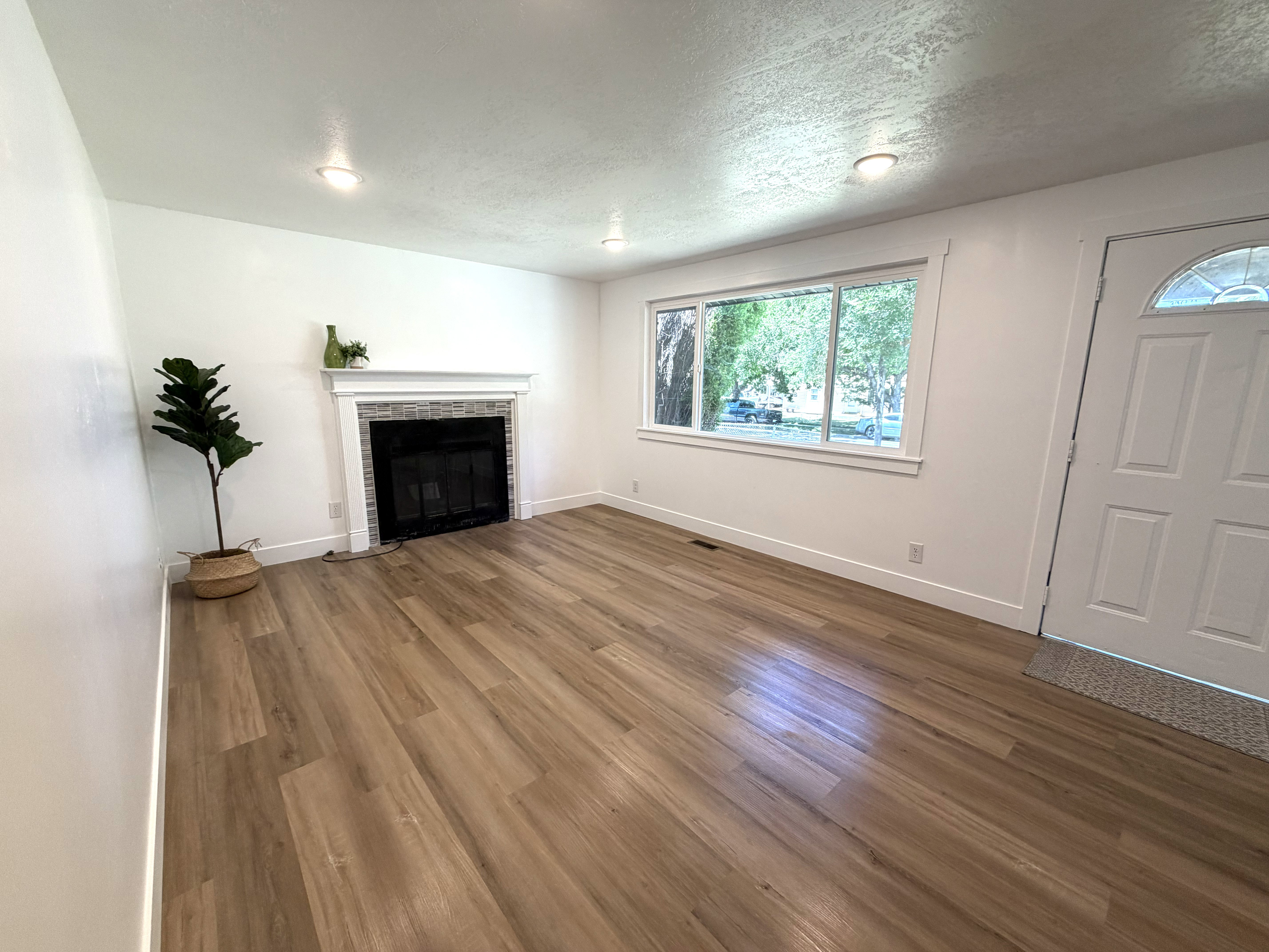 Spacious living area featuring wood-finish flooring, a fireplace with a decorative mantel and tiled surround, recessed lighting, and a multi-pane window