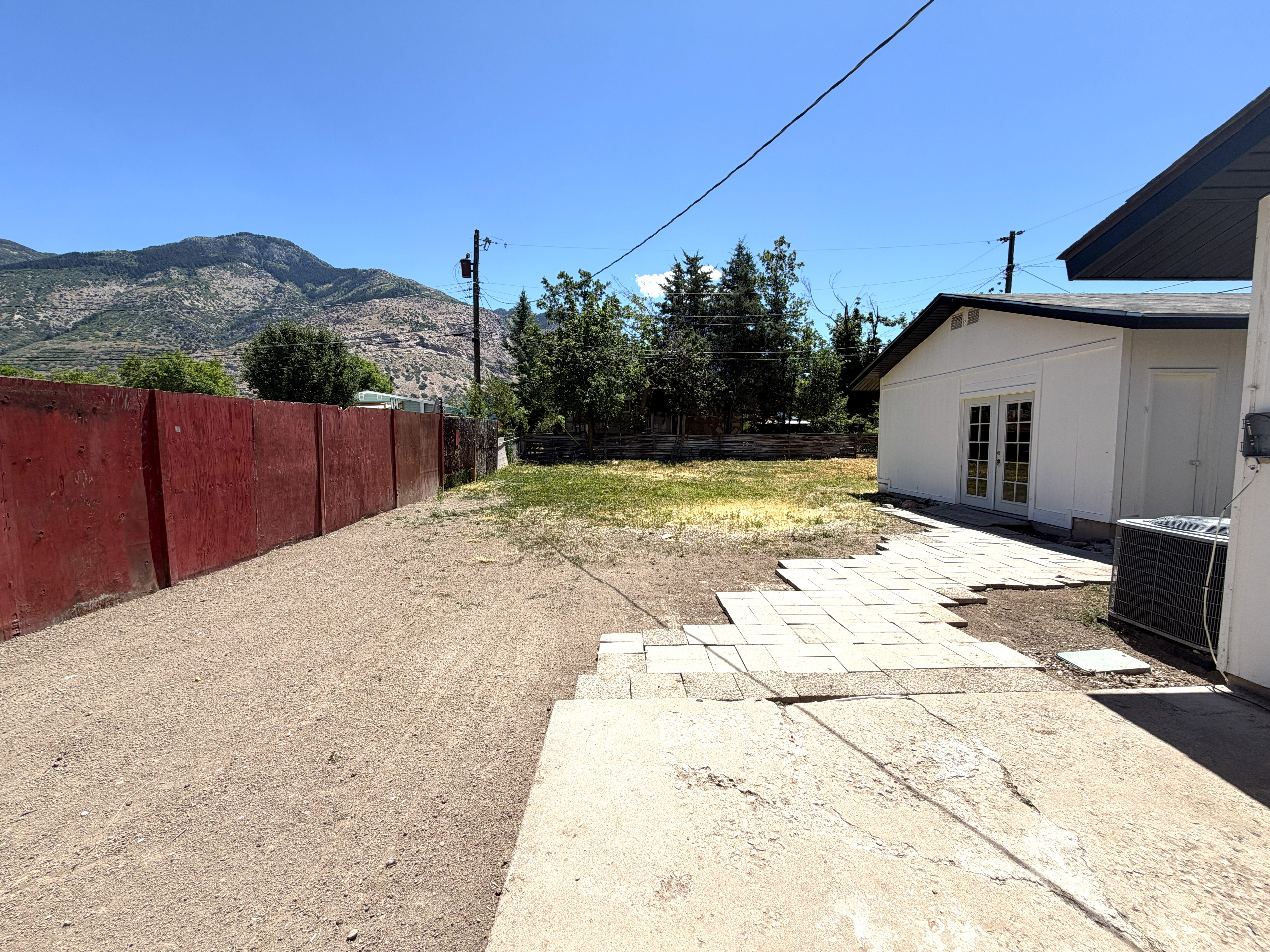 Spacious backyard area featuring a concrete patio, a paver stone pathway, and a red perimeter fence