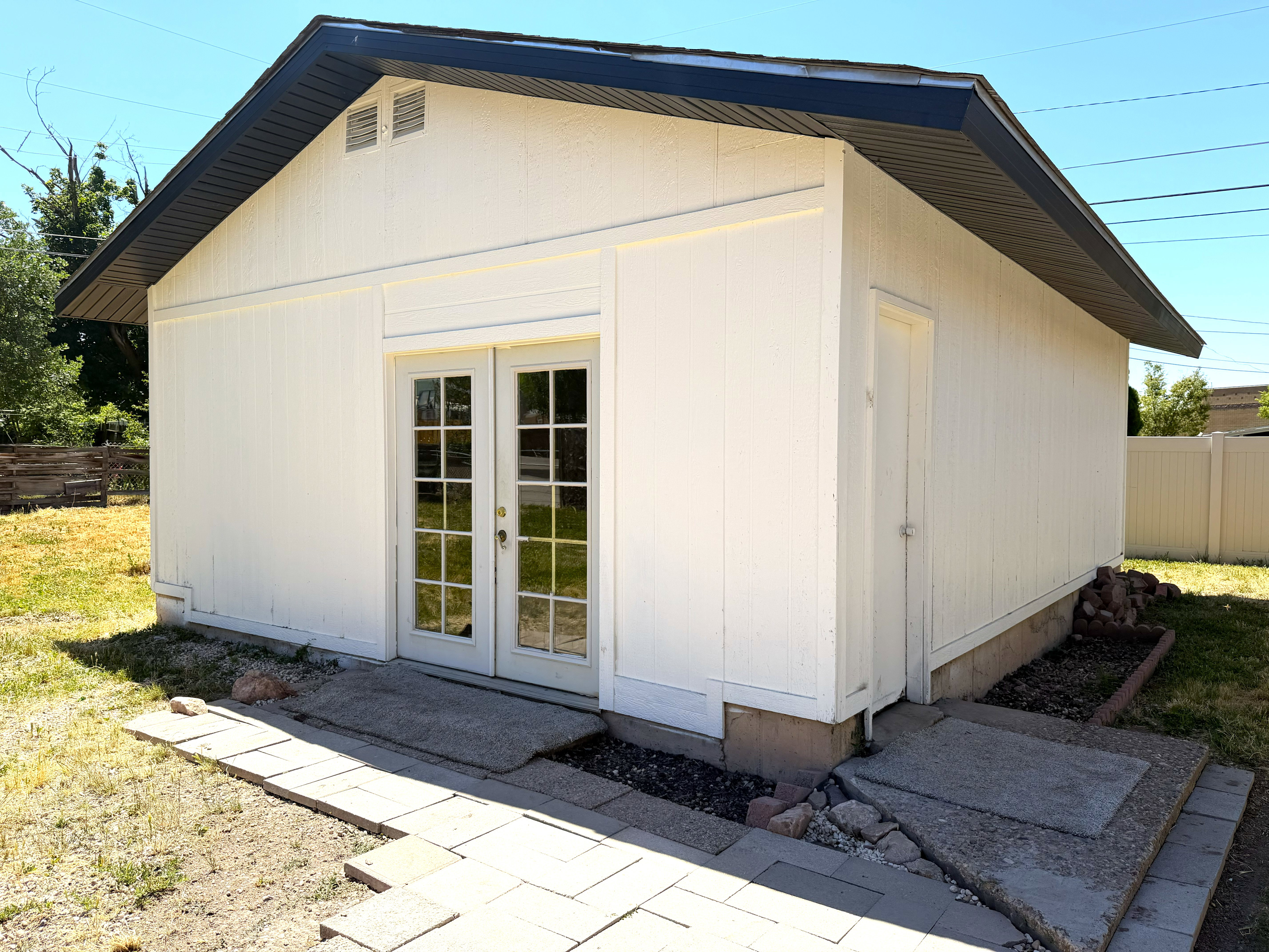 White-painted outbuilding featuring a dark-toned roofline, double glass-paneled doors, and an additional single entry door