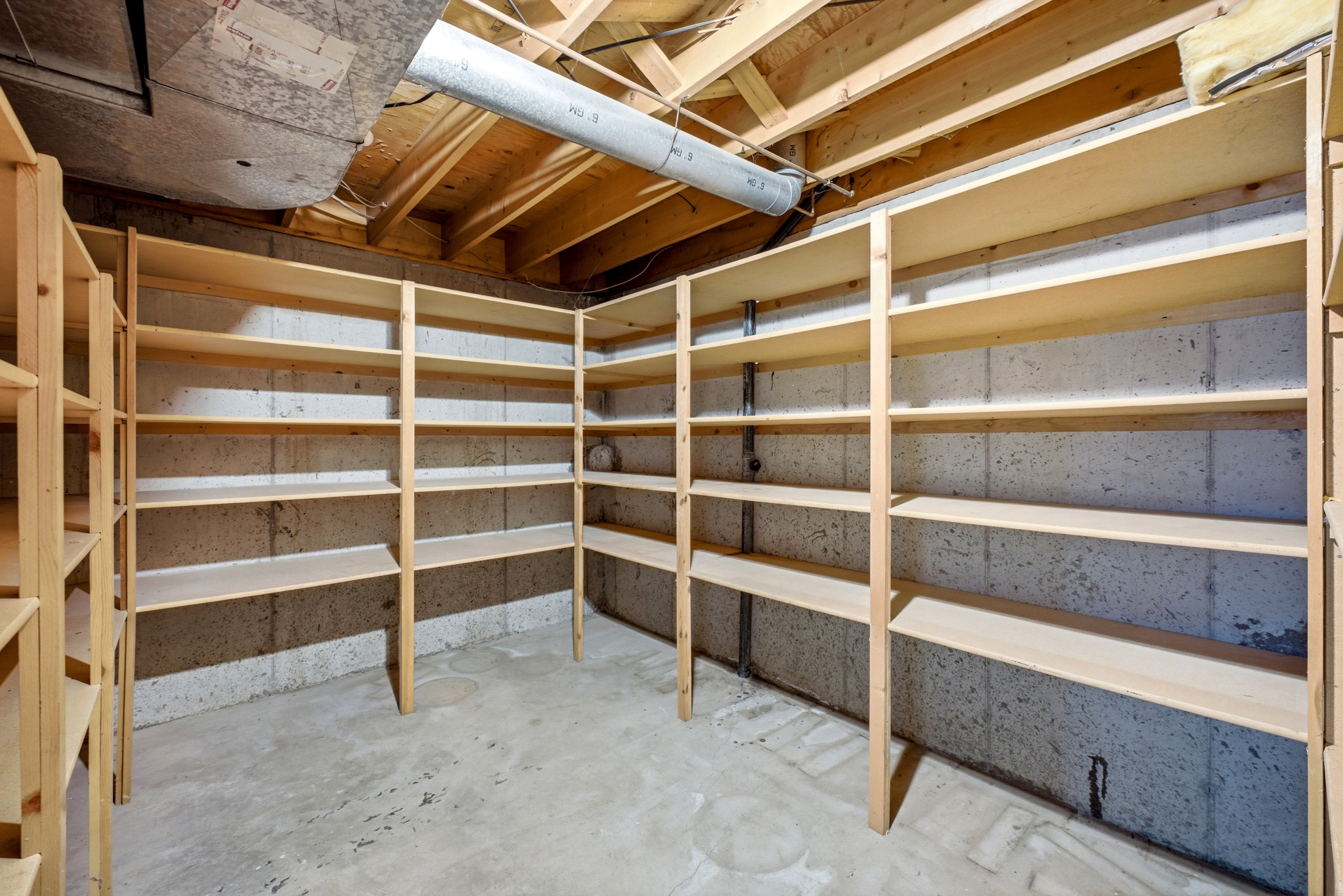 Storage area featuring extensive built-in wooden shelving, concrete block walls, and a concrete floor