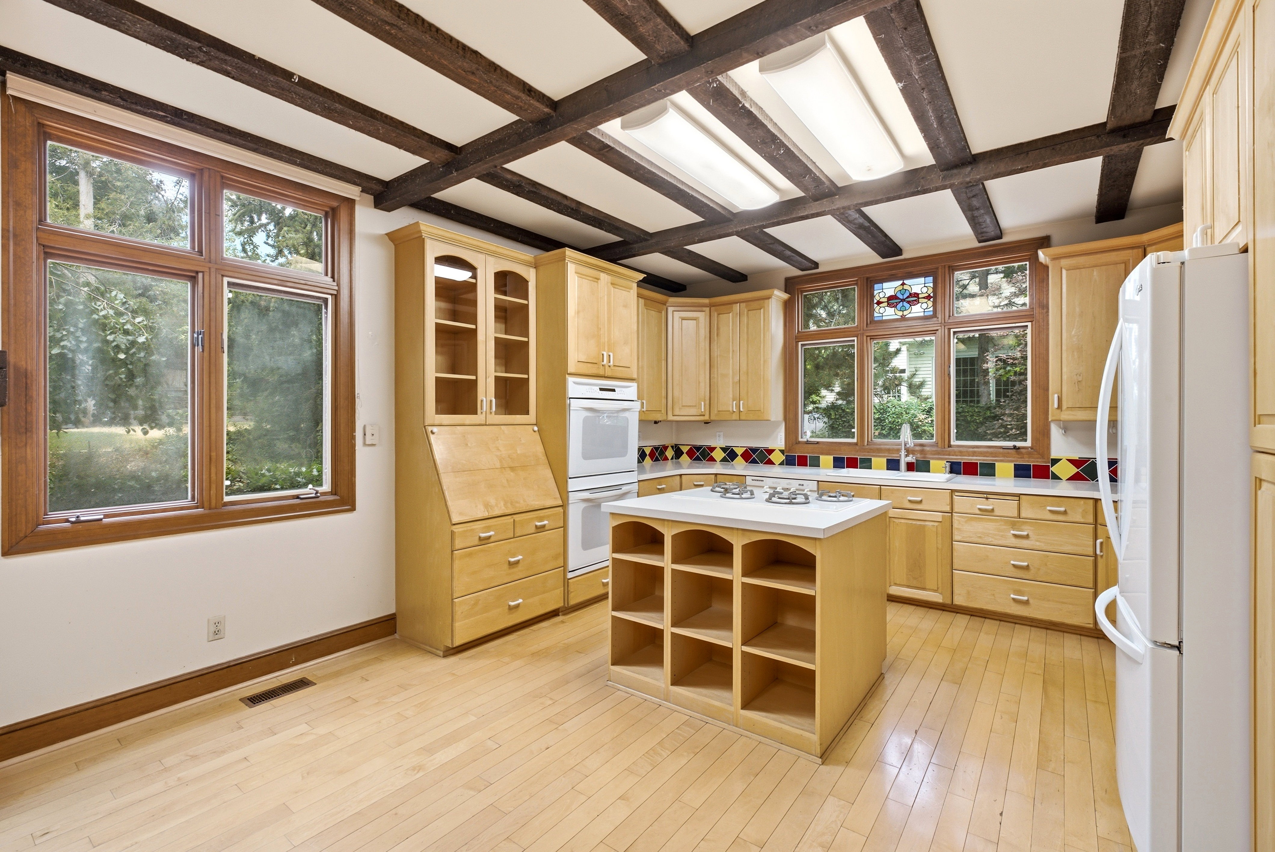 Kitchen featuring light wood cabinetry, exposed beam ceiling, wood-finish flooring, white countertops, and a central island with cooktop