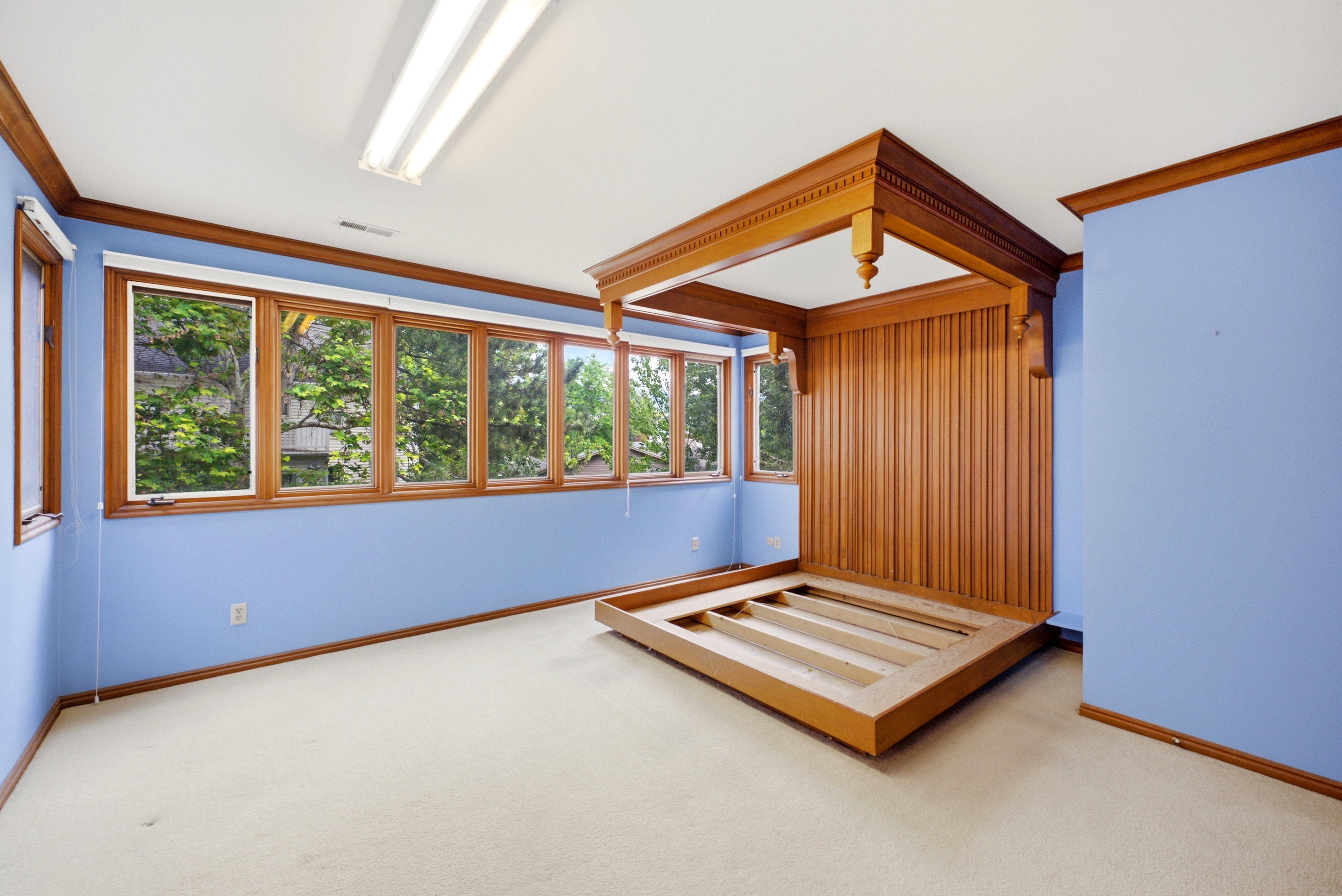 Room featuring a large window bank, light blue walls, and a built-in wood-paneled headboard with decorative trim