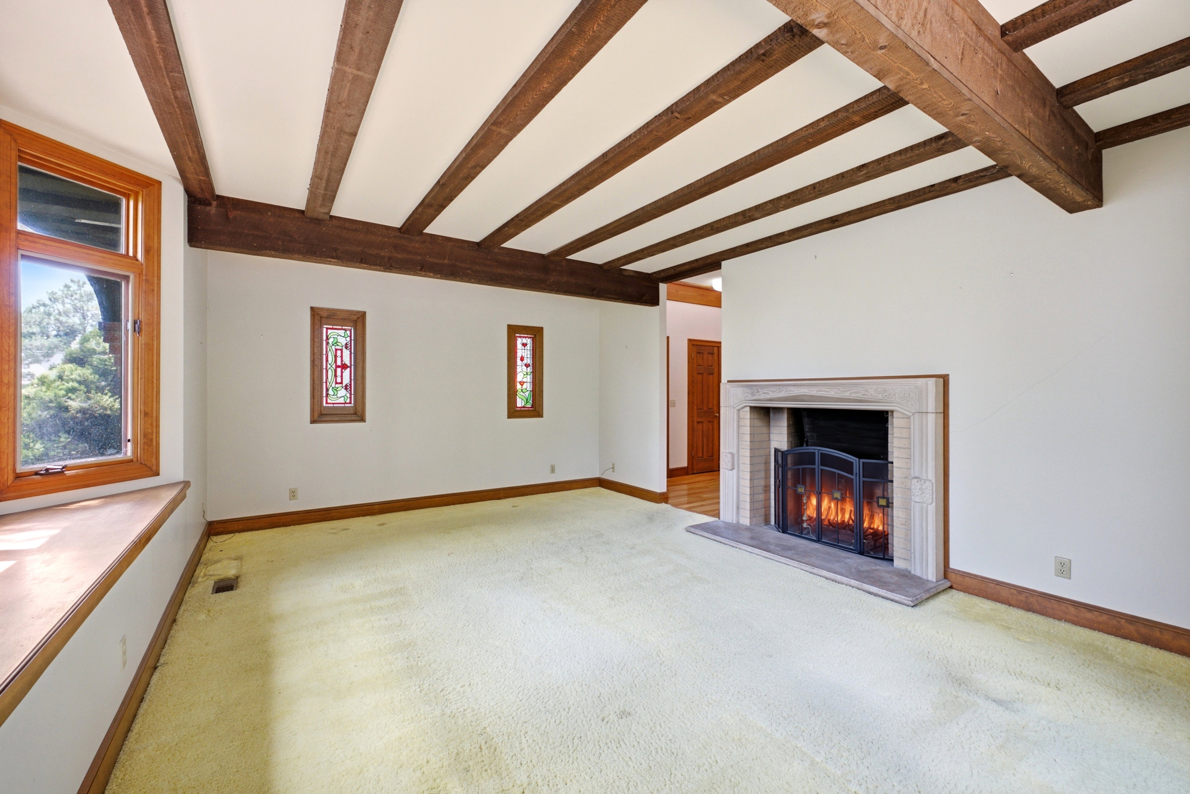 Exposed wood ceiling beams define this room, featuring a built-in stone fireplace with a hearth