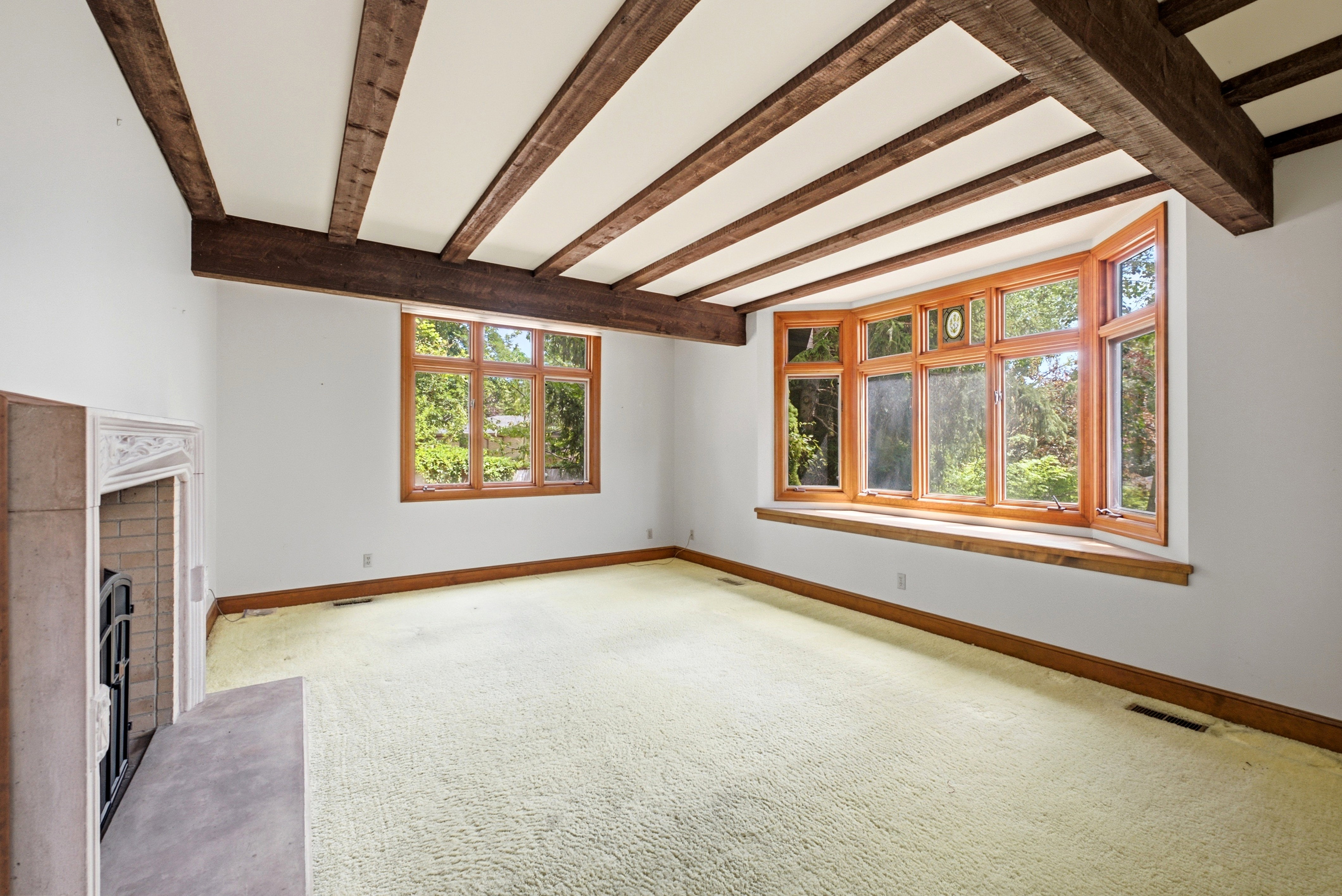 Room featuring exposed ceiling beams, a decorative fireplace with an ornate mantel, and a large bay window with wood framing and a built-in sill