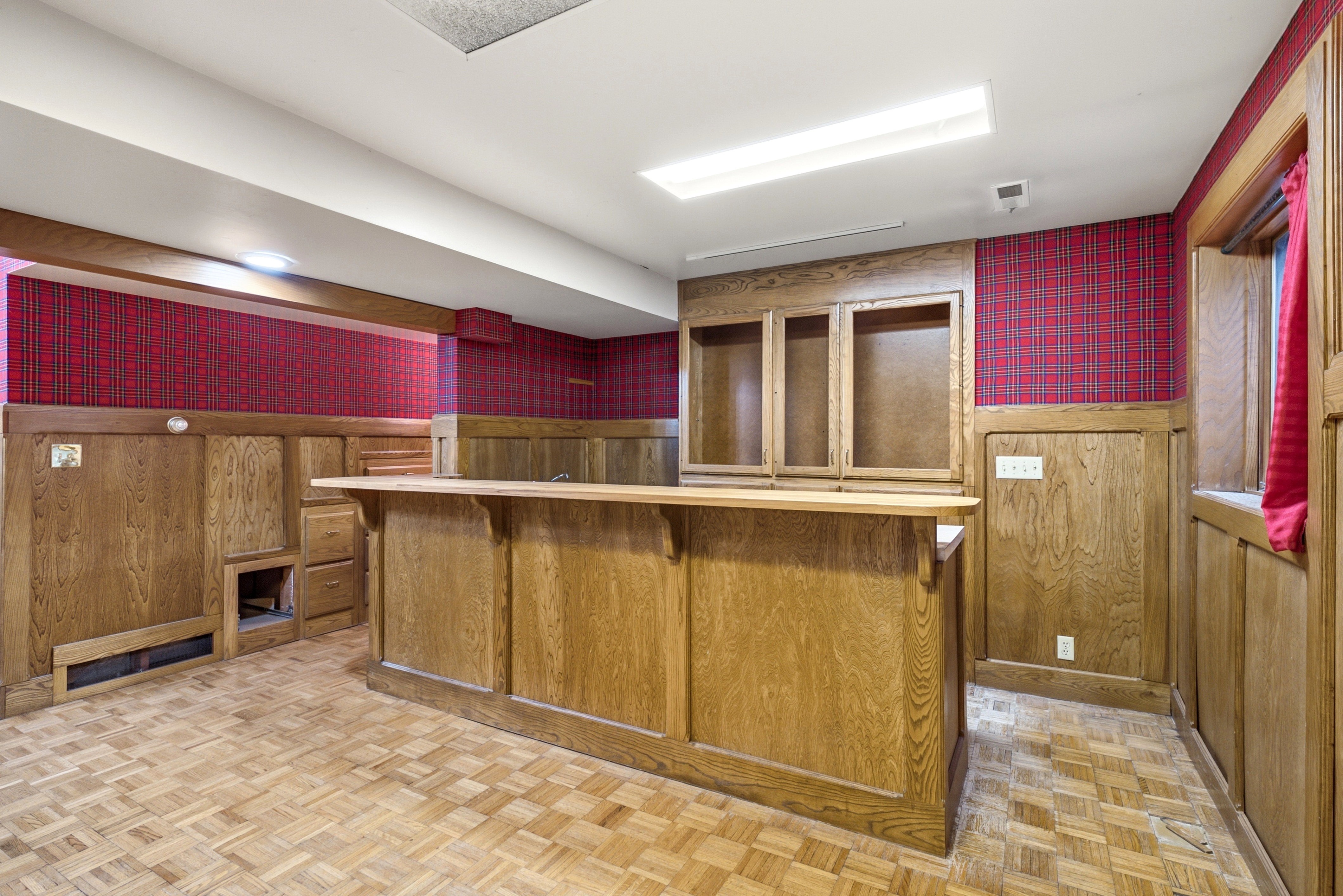 Recreation room featuring a built-in wood-finish bar with integrated cabinetry and shelving, parquet wood flooring, and wood paneling with patterned wallpaper accents