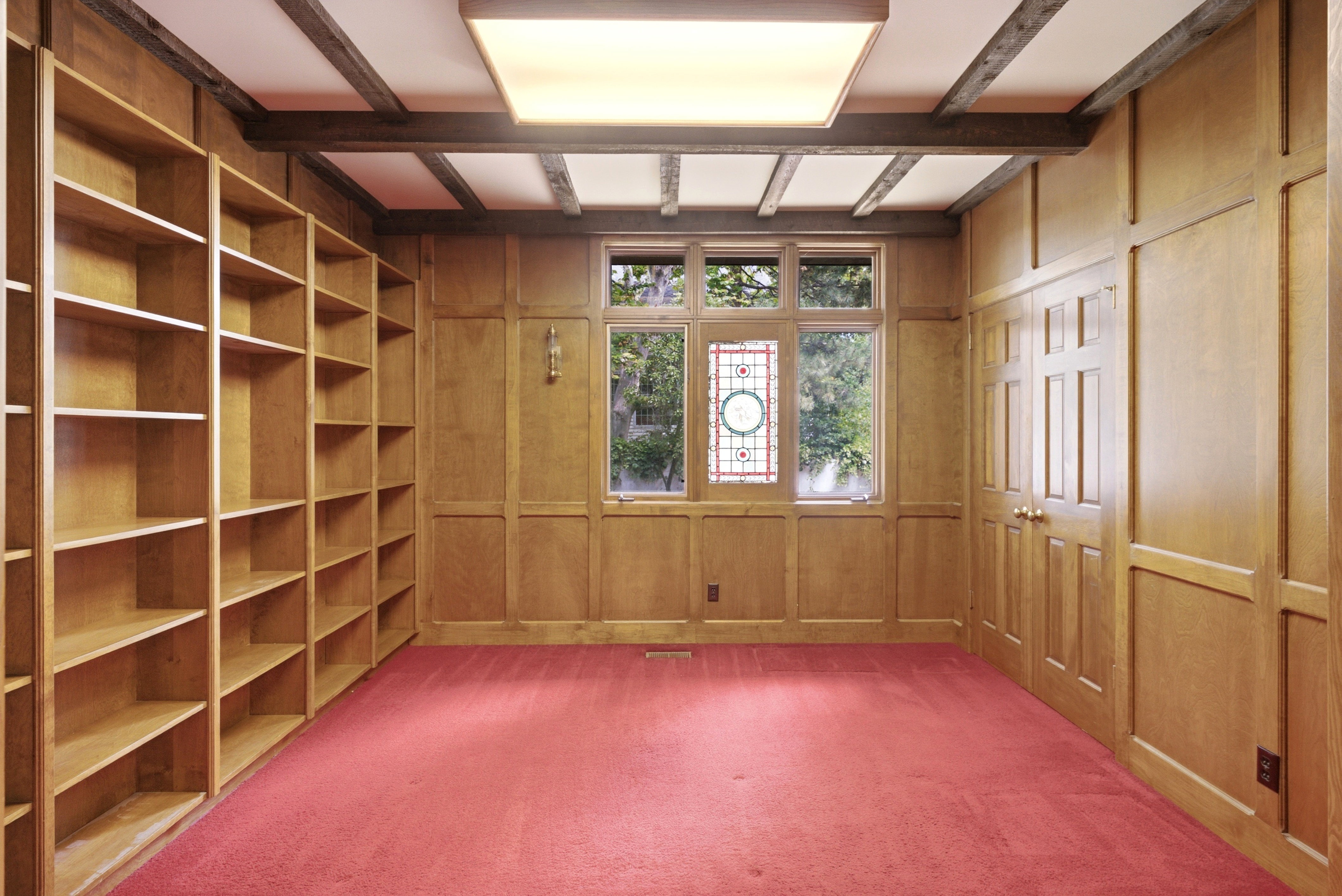 Room featuring extensive wood paneling, built-in shelving, and a coffered ceiling with exposed wood beams