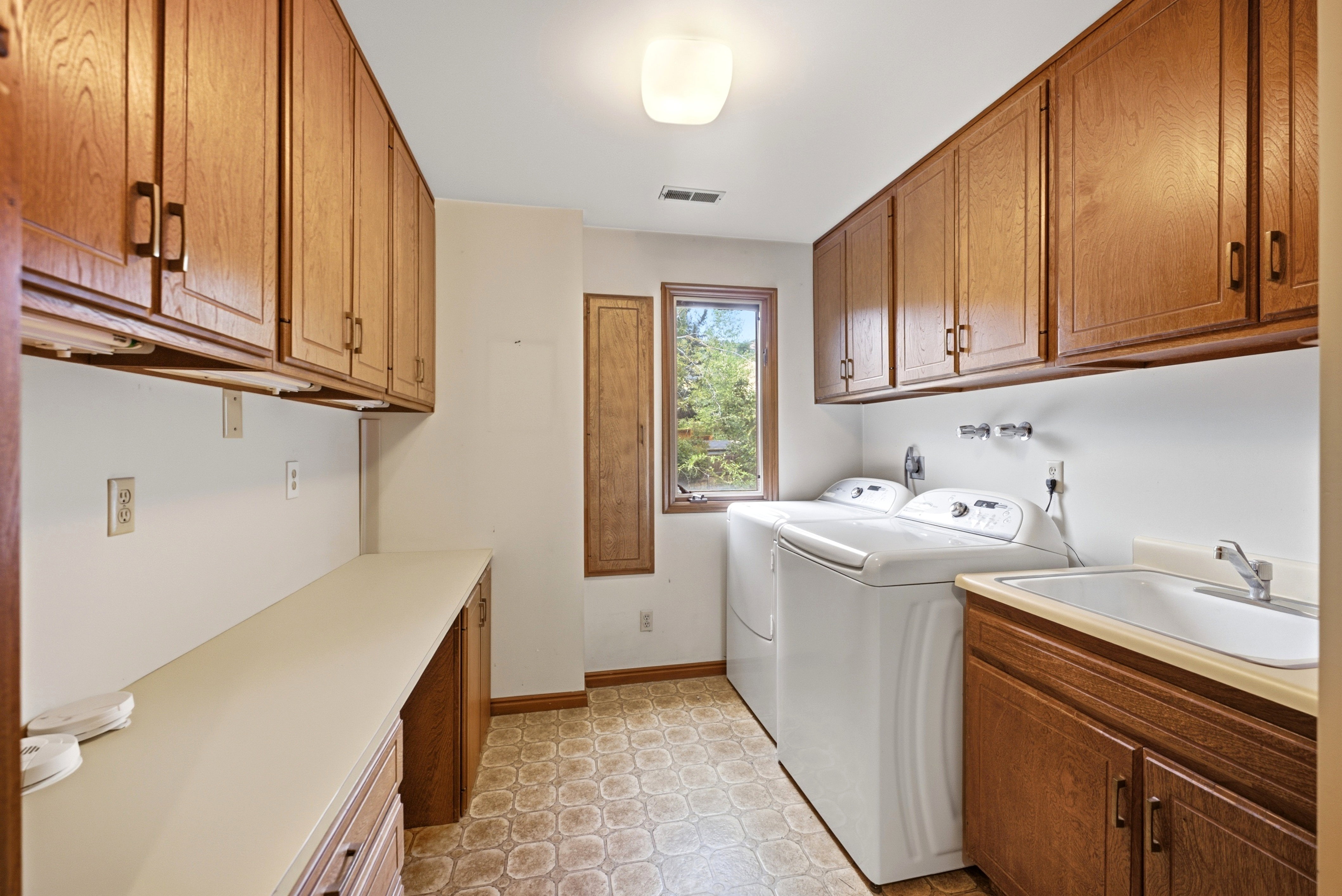 Laundry room featuring extensive wood cabinetry, a utility sink with a faucet, a window with exterior views, and patterned floor tile