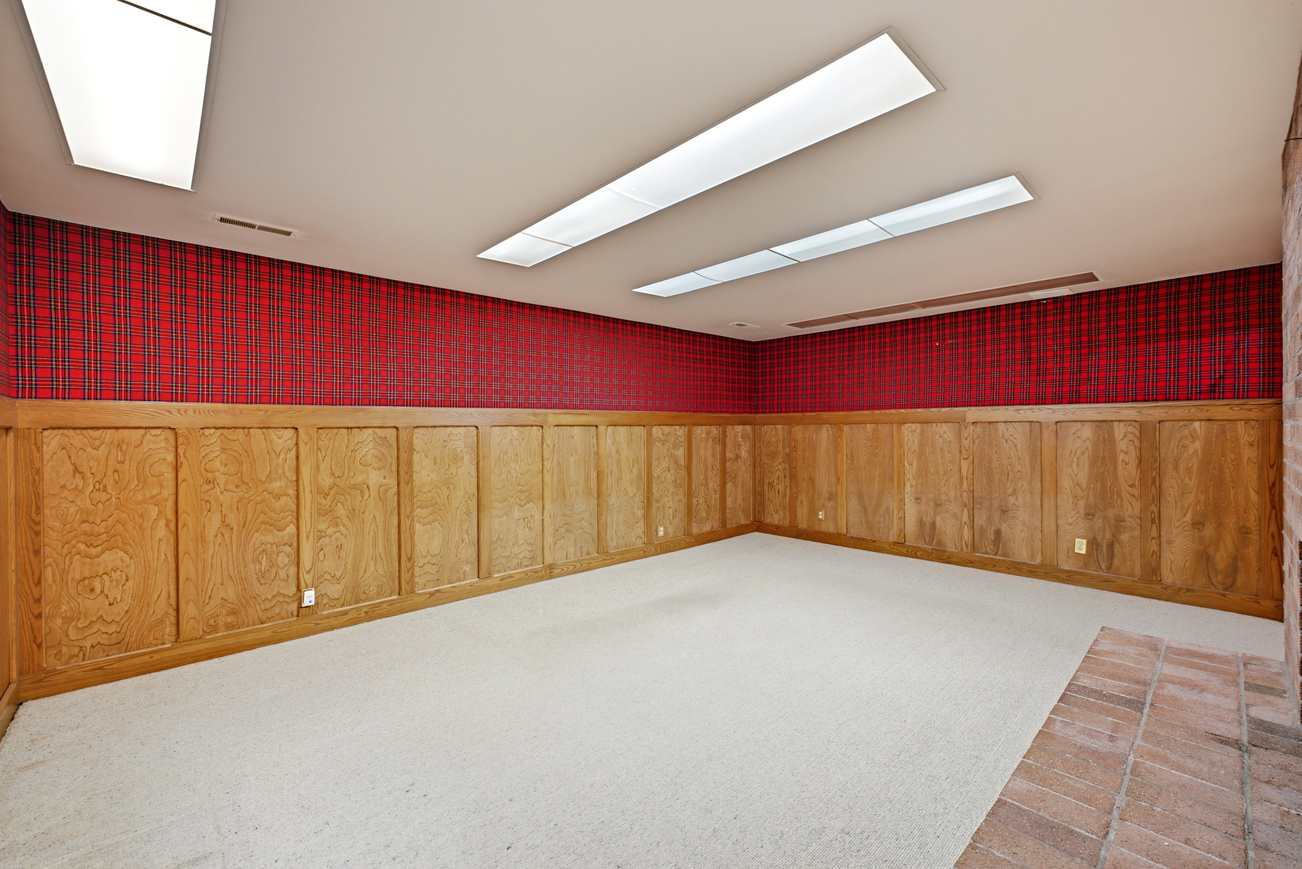 Spacious room featuring wood paneling, plaid wallcovering, and light-colored carpeting