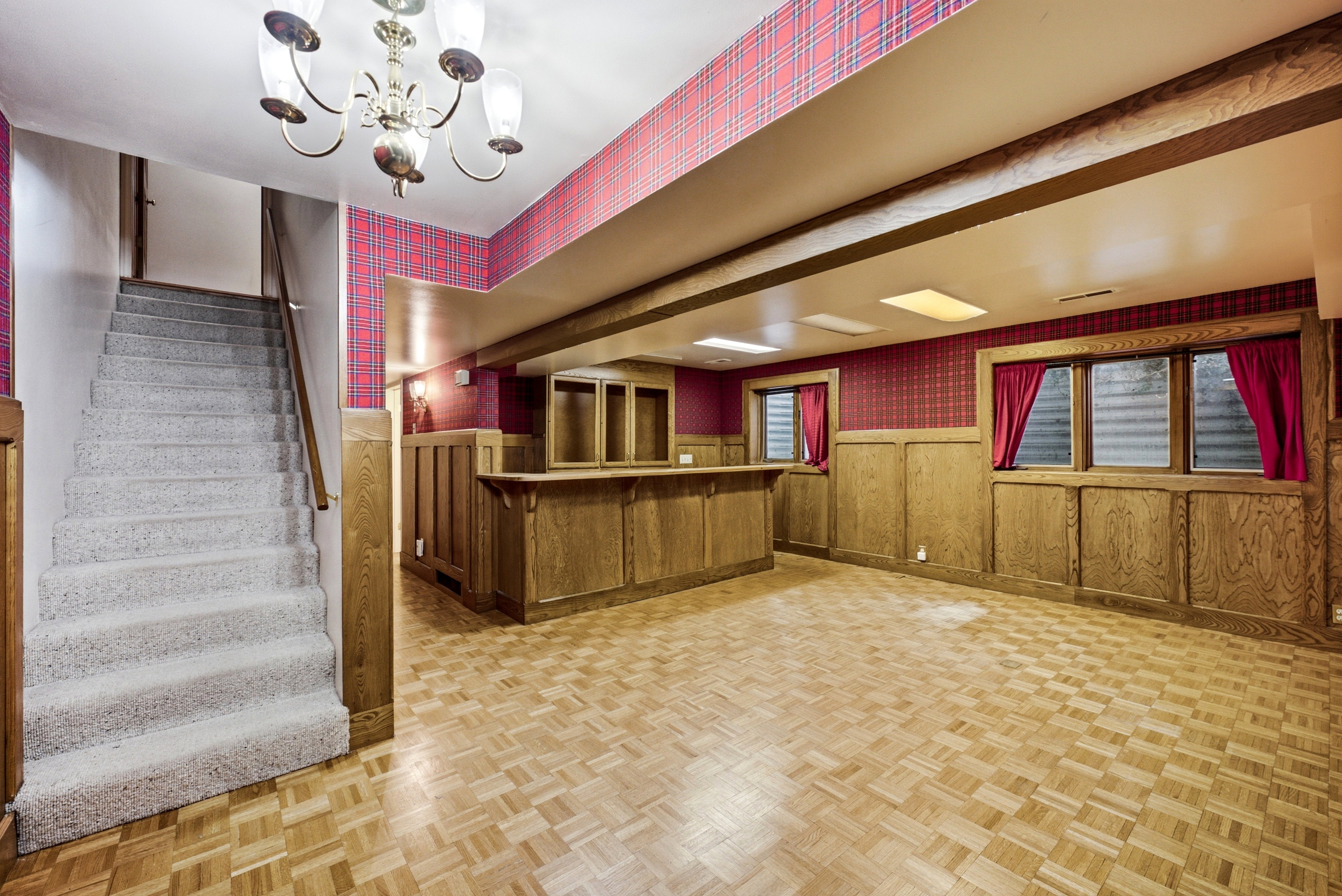 Spacious lower level featuring wood-finish flooring, a built-in bar, wood paneling, and an overhead chandelier