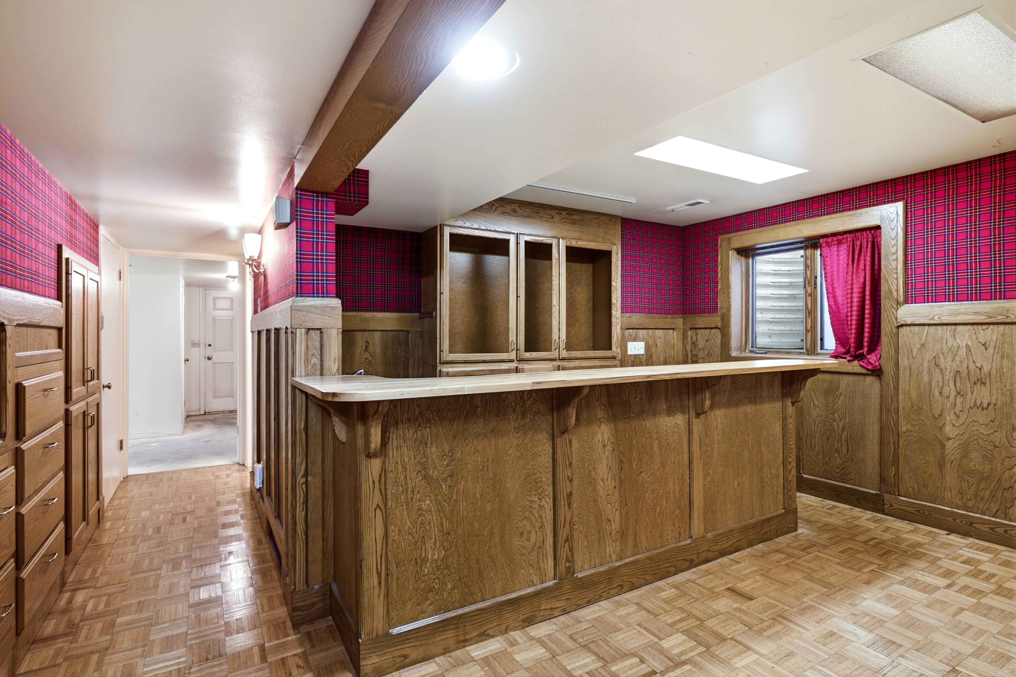 Built-in wooden bar with integrated shelving, complemented by wood-finish flooring and plaid wall covering