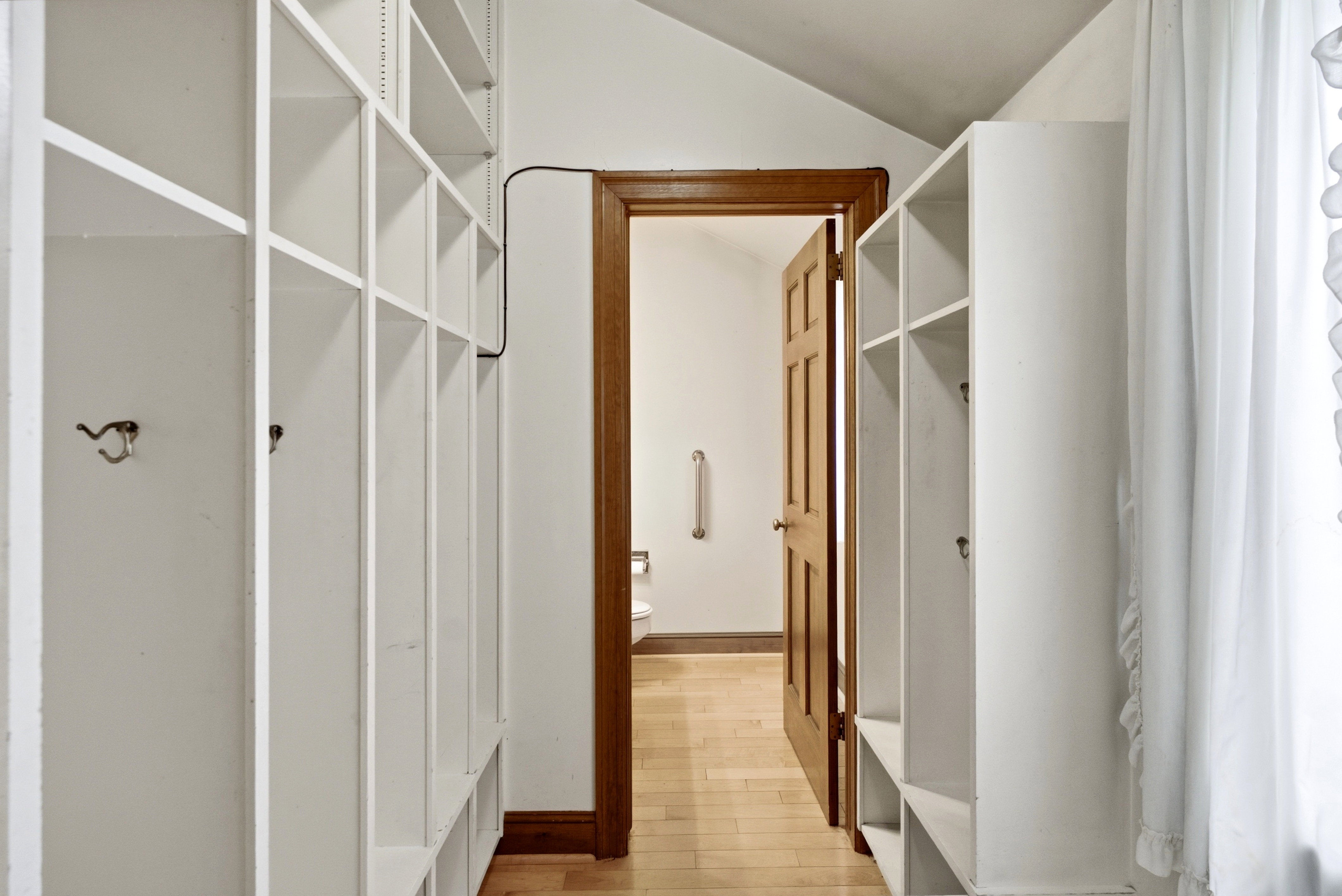 Hallway featuring built-in white shelving units, wood-finish flooring, and a wood-paneled door
