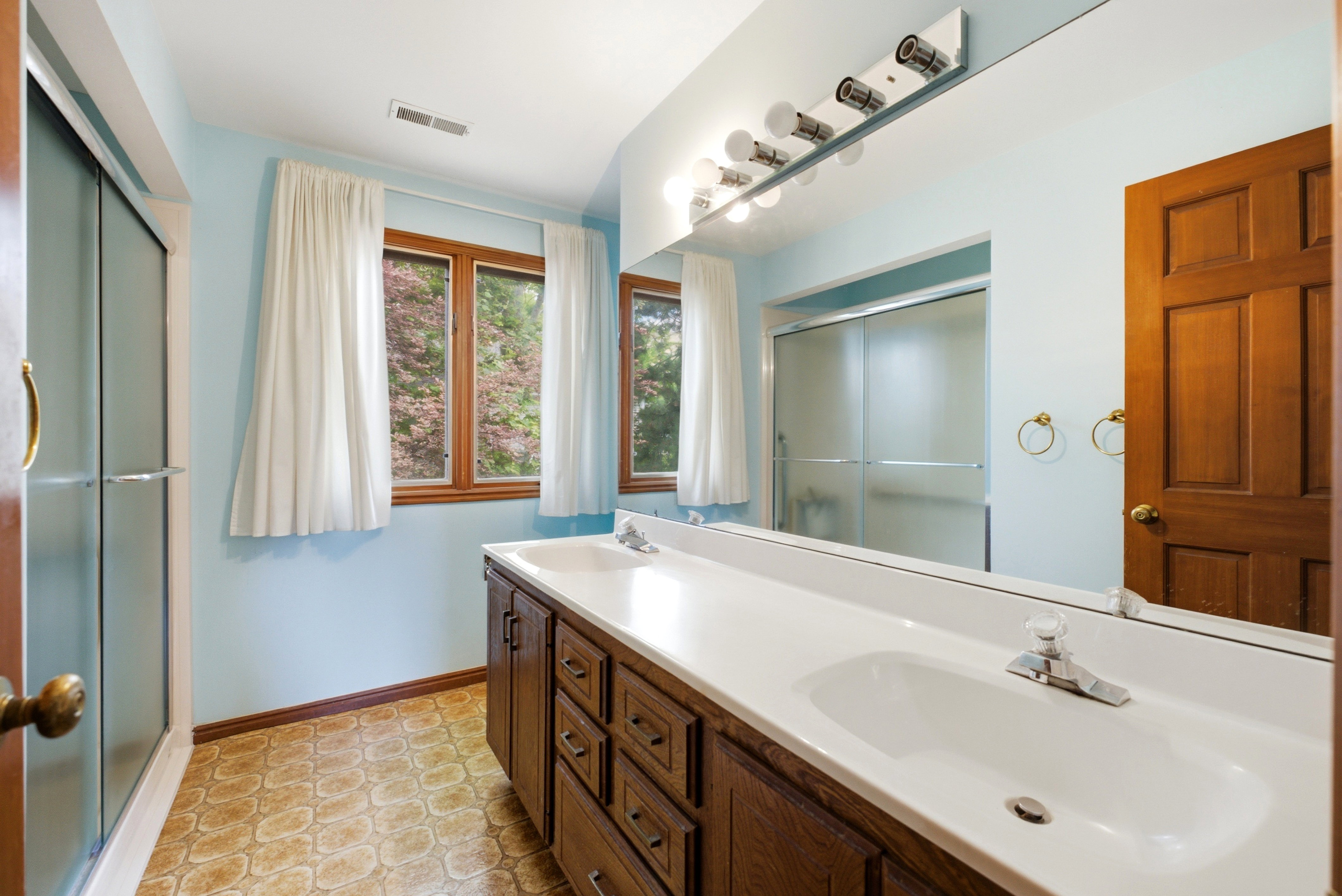 Bathroom featuring a dual vanity with a white countertop and integrated sinks, wood-finish cabinetry, and a full-width wall mirror