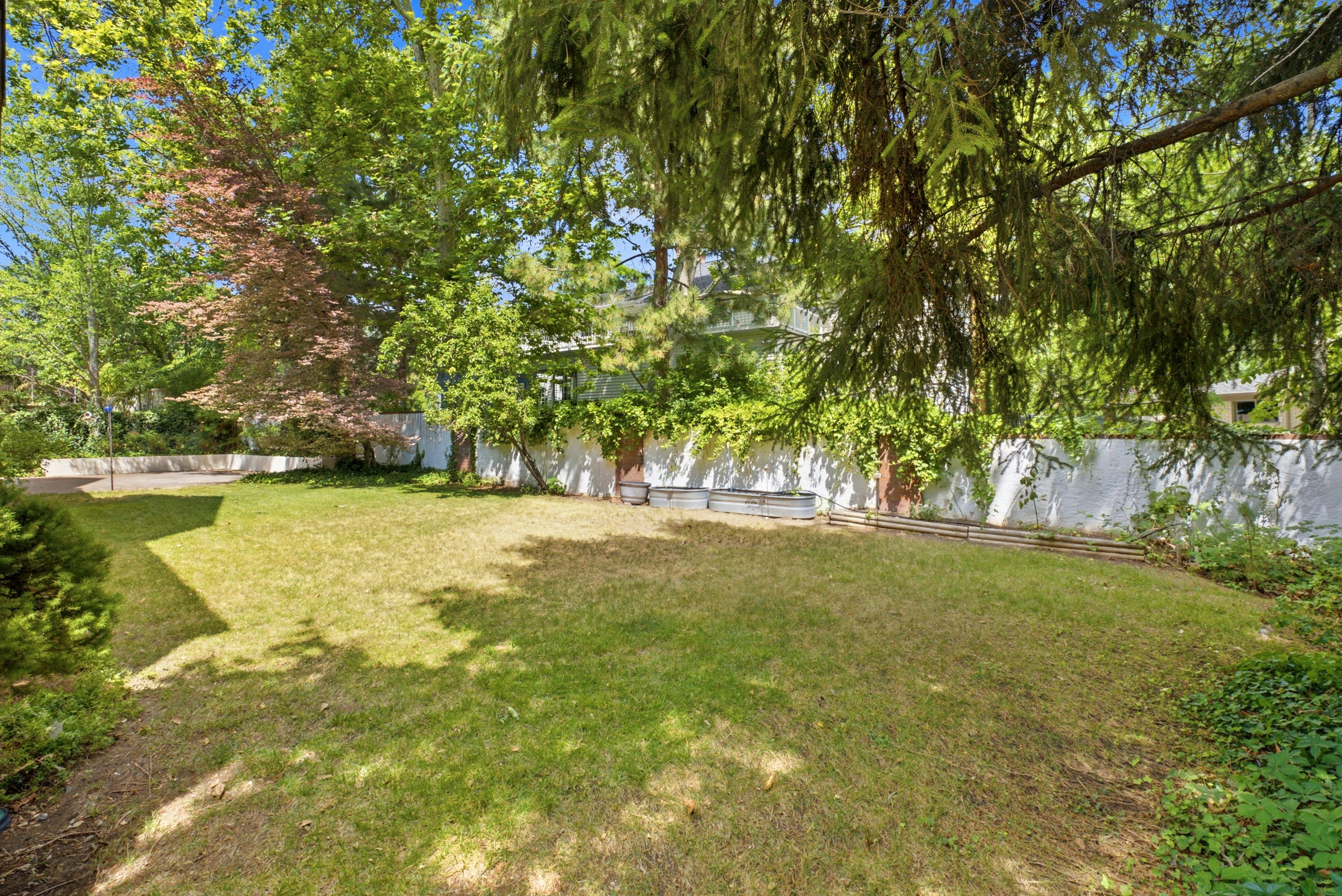 Expansive grassy yard with mature trees and a perimeter fence