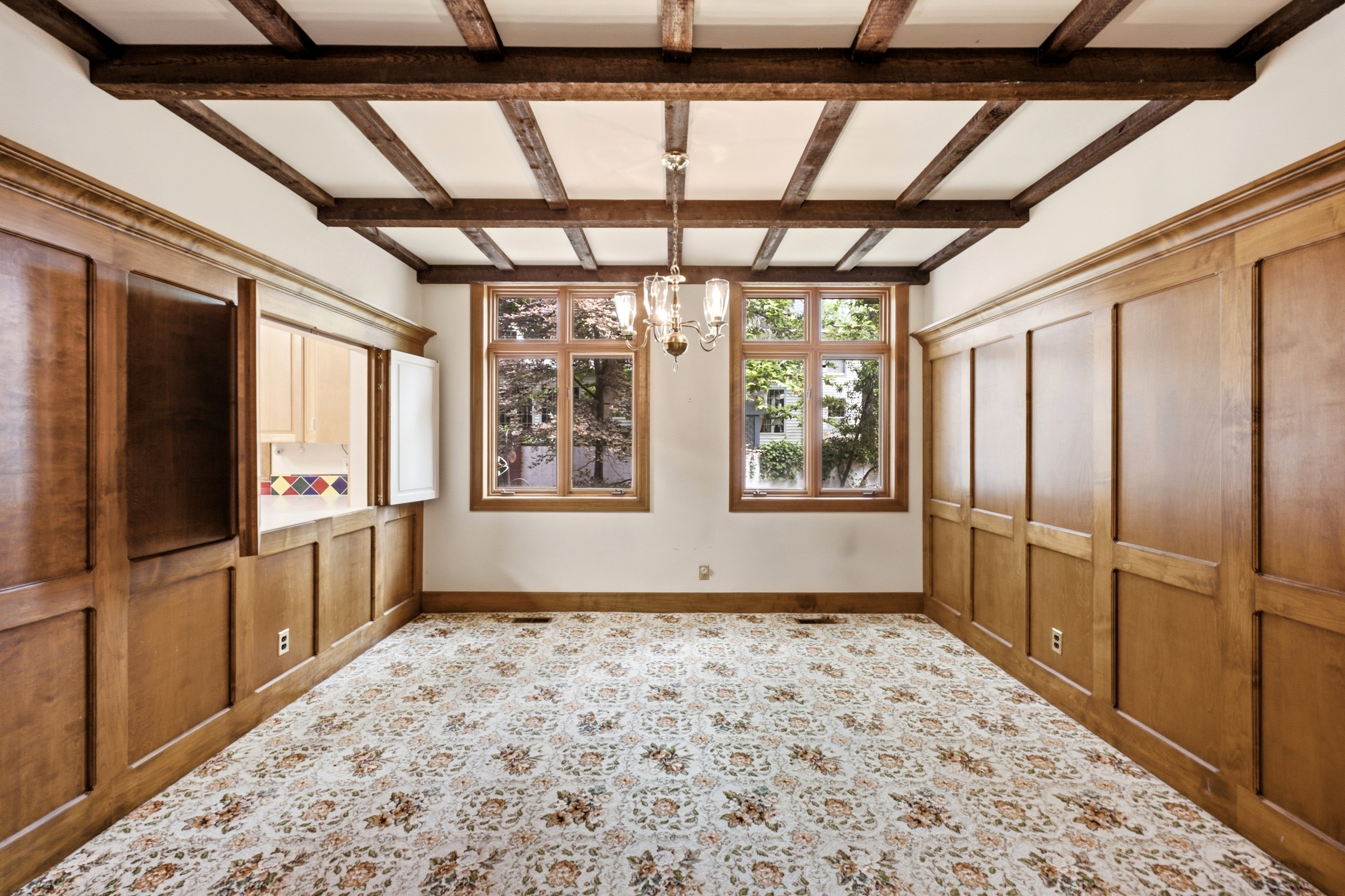 Room featuring wood paneling, wood-frame windows, a coffered ceiling with wood beams, and a pass-through window with light-toned cabinetry