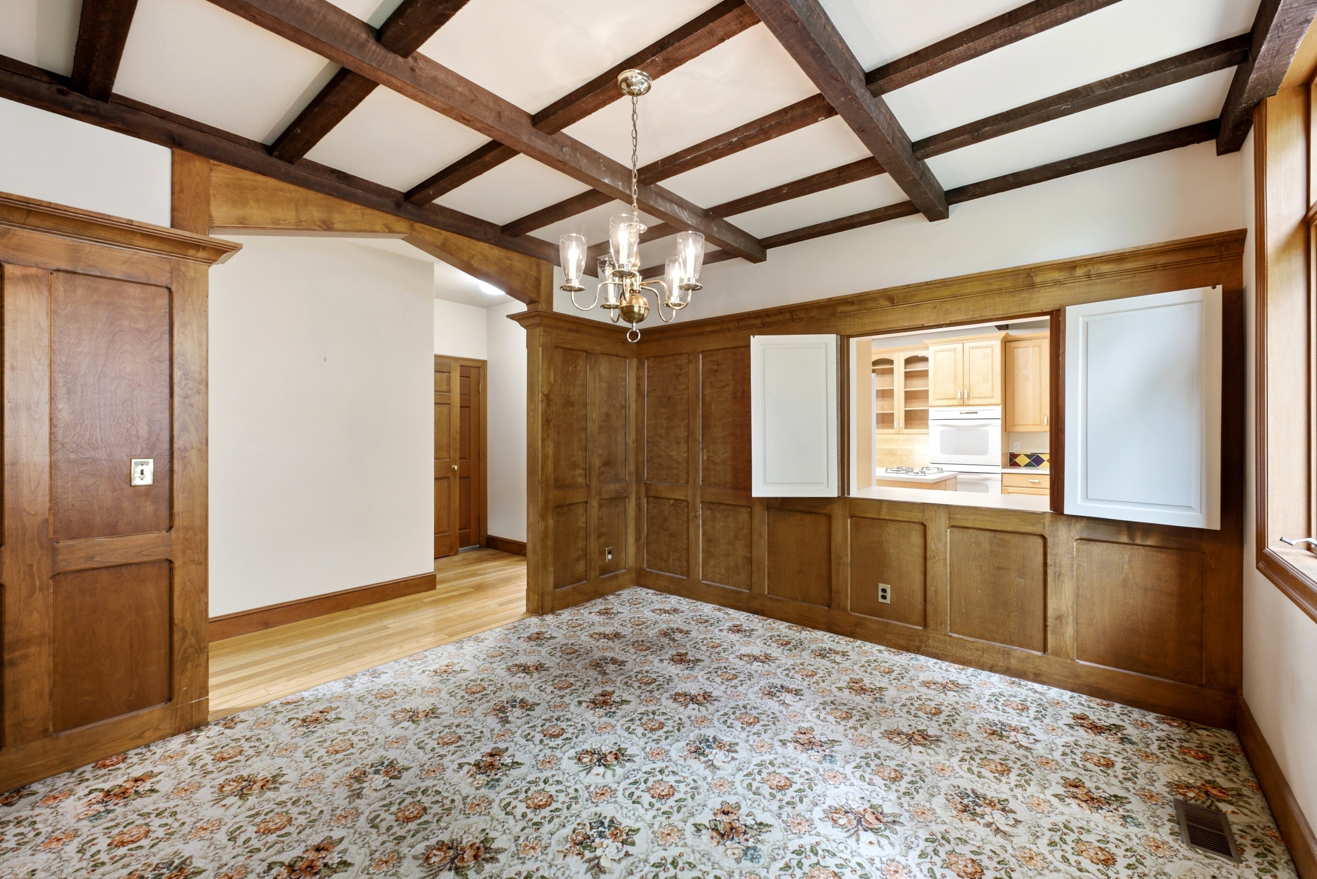 Room featuring wood-paneled walls, exposed ceiling beams, and a decorative chandelier
