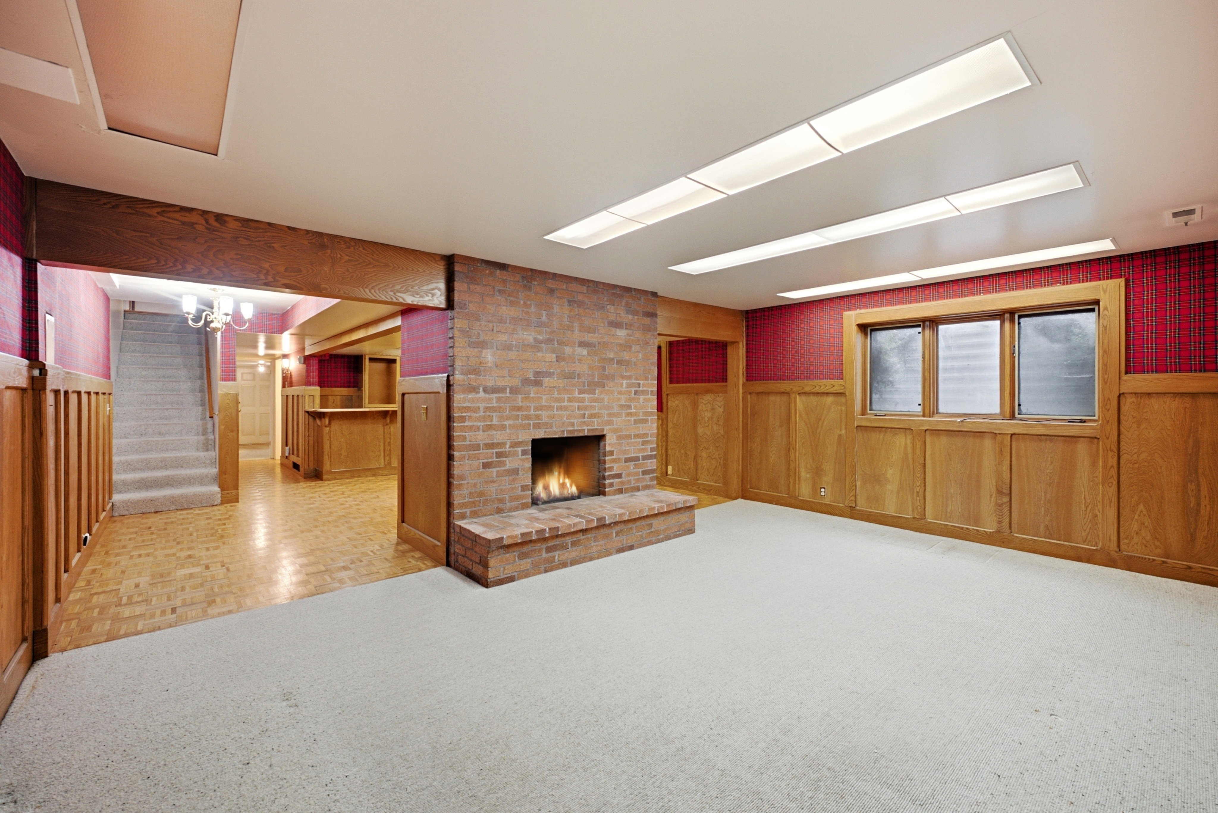 Spacious room featuring a brick fireplace, light-toned carpeting, and wood-paneled walls