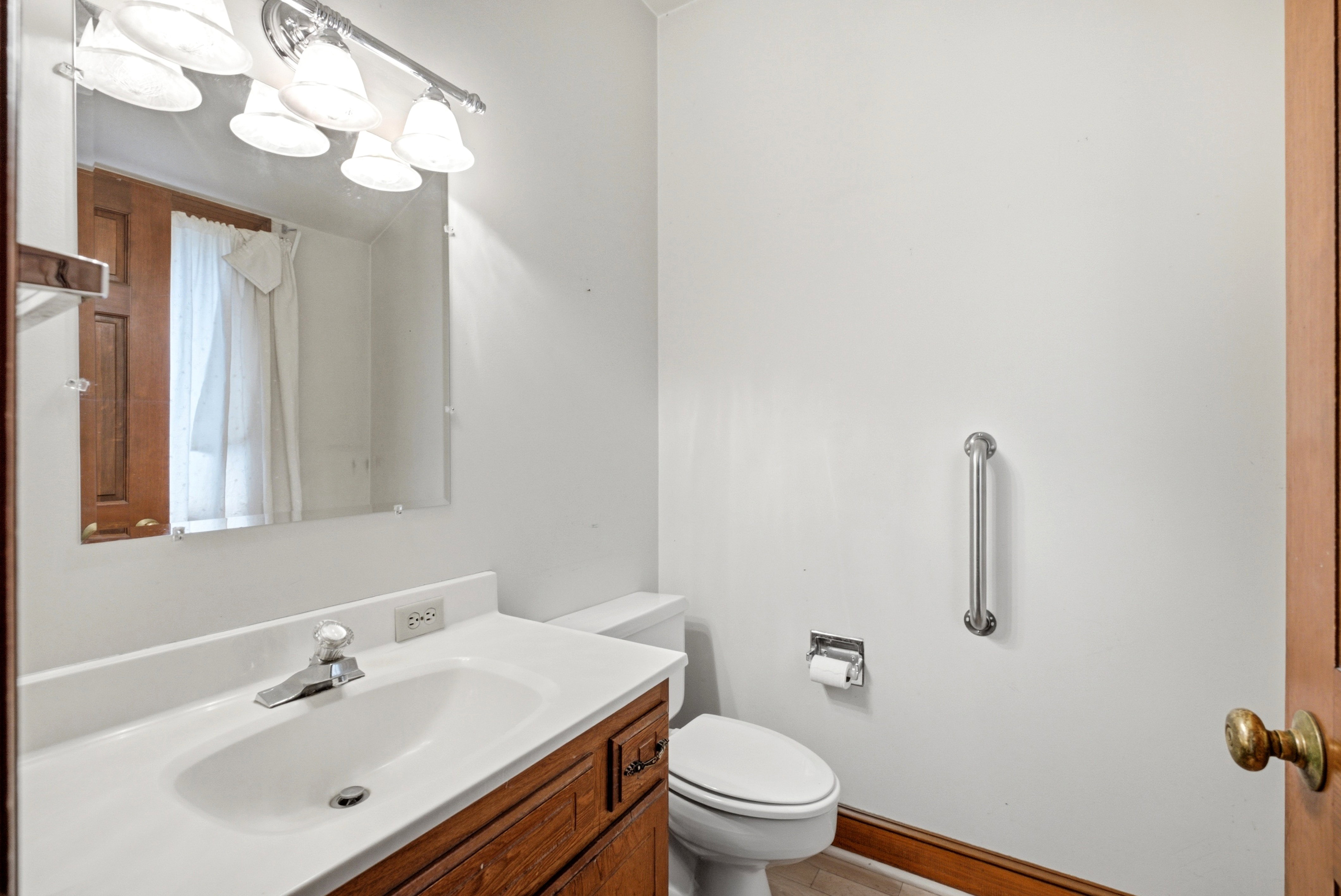 Bathroom featuring a wood-finish vanity with a white countertop and integrated sink, a wall-mounted mirror, and a four-bulb vanity light fixture