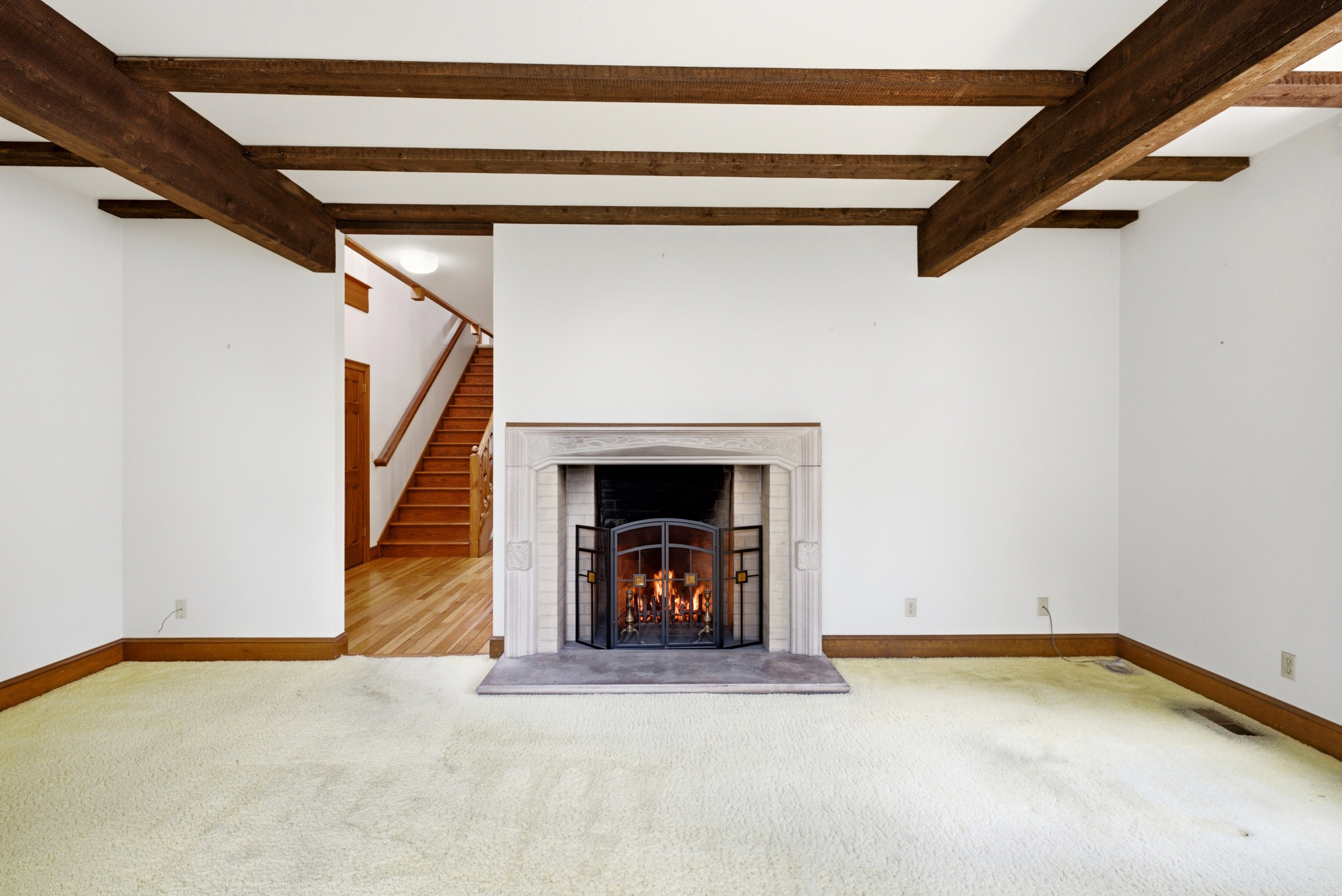 Room featuring exposed wood ceiling beams, a stone fireplace with a metal screen, white walls, and wood trim flooring