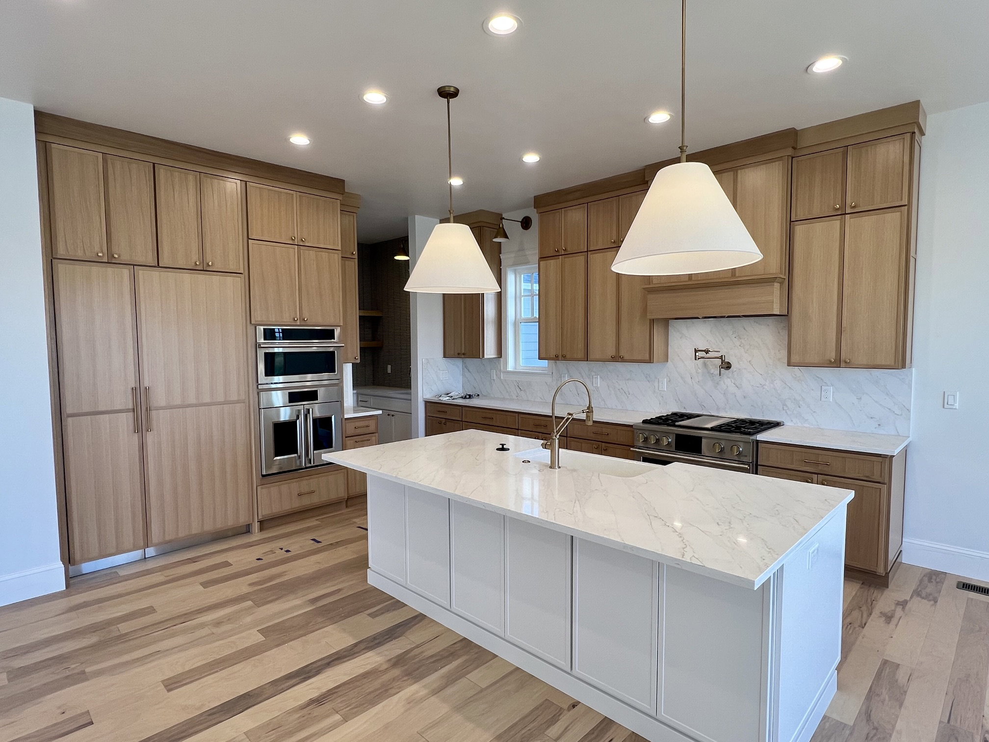 Gourmet kitchen featuring a substantial island with a white countertop, light wood-finish cabinetry, integrated paneled refrigerator, stainless steel double ovens, and a gas range with a pot filler