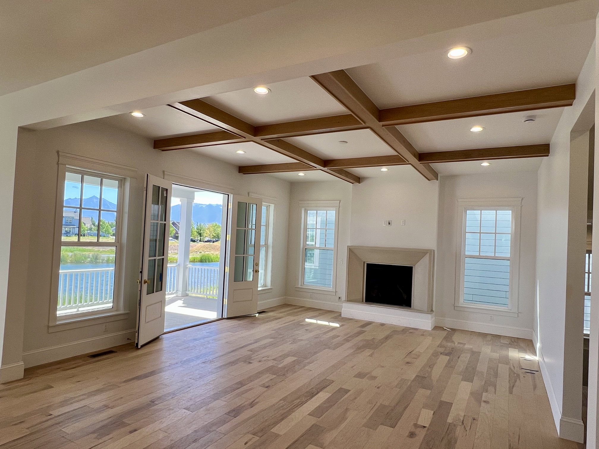 Spacious room featuring coffered ceilings with recessed lighting, light wood-finish flooring, and a stone fireplace